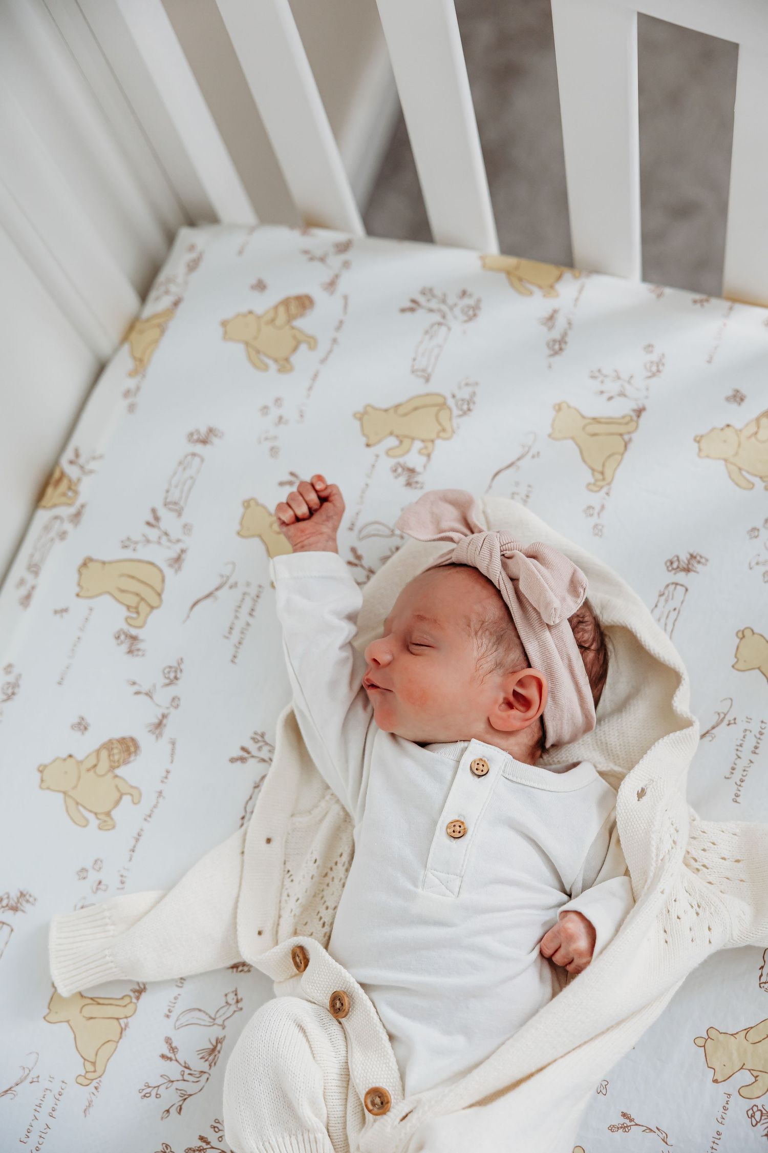 Newborn baby sleeping peacefully in white crib with animal print bedding.