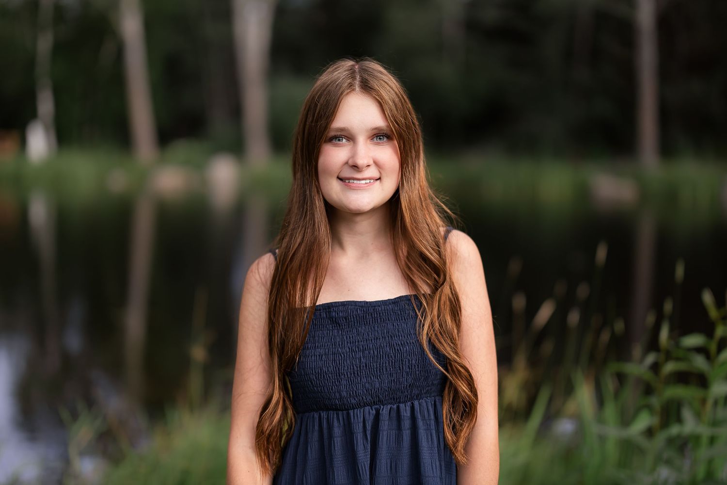 Portrait in navy dress with natural lake and foliage background.