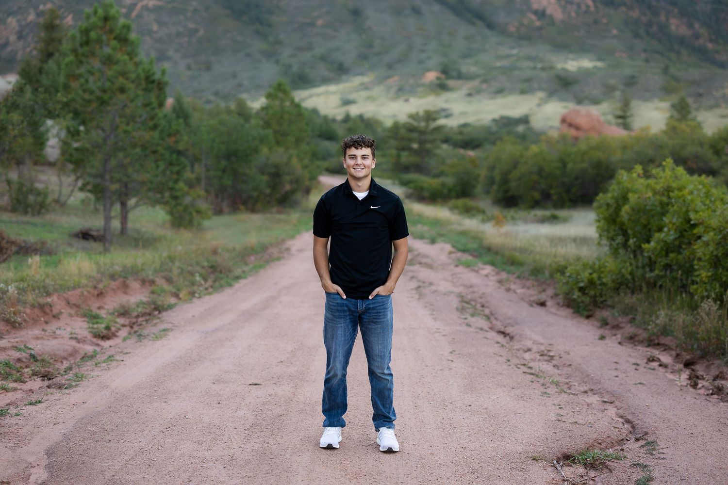 Person walking on a scenic mountain trail surrounded by rugged terrain and green vegetation.