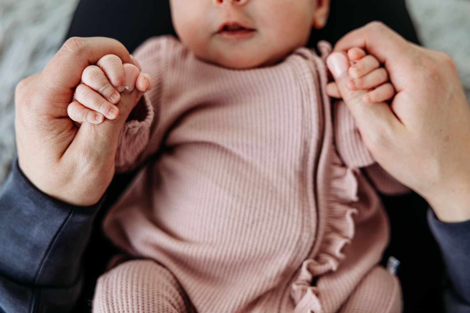 Baby wearing pink ribbed outfit lying on soft fabric.