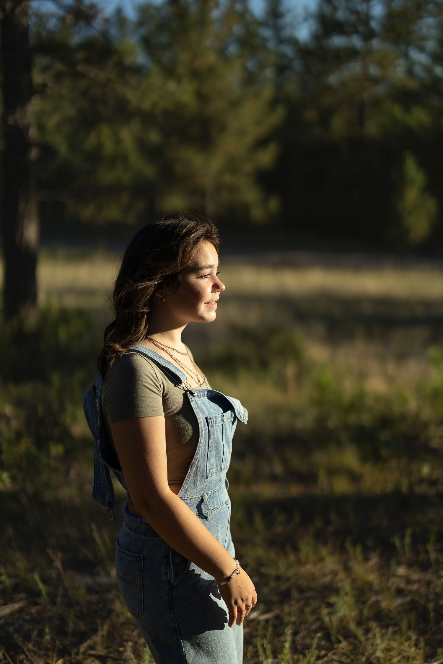 Person in overalls standing in field during golden hour lighting.