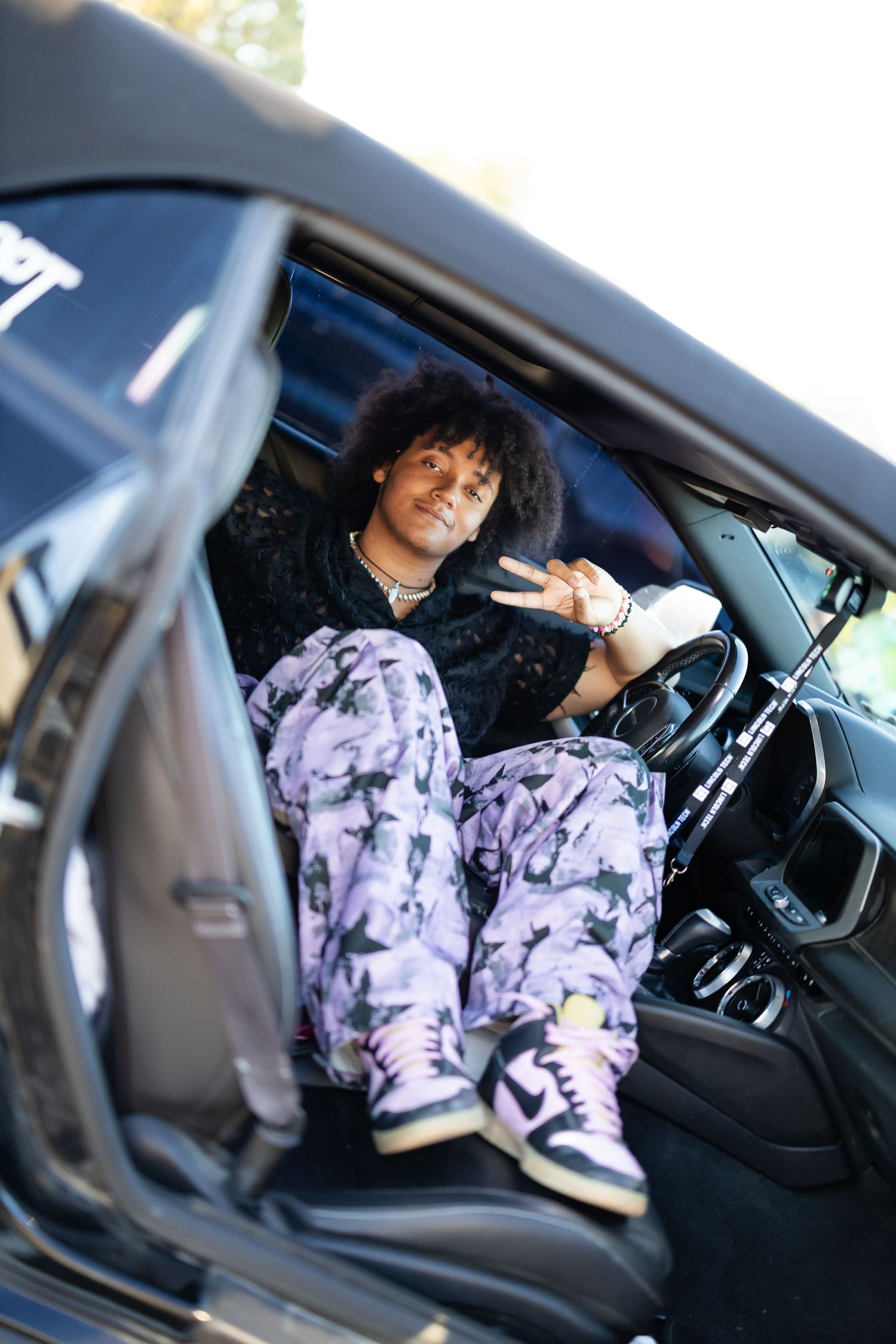 Person in purple tie-dye hoodie sitting in driver's seat of car.