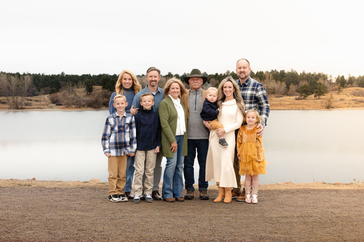 Family group portrait by lake wearing coordinated casual outfits.