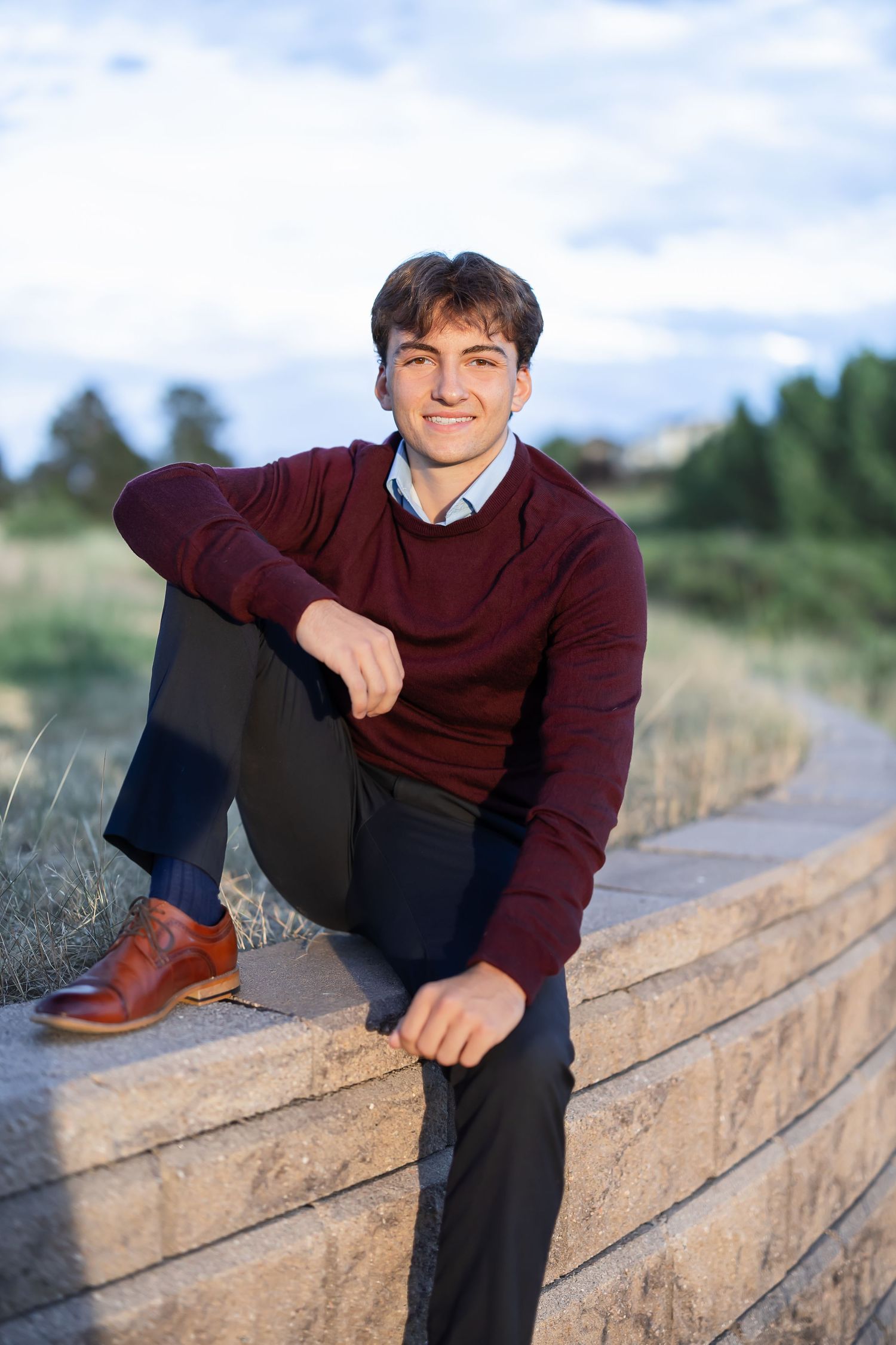 Young person in maroon sweater sitting casually on concrete ledge outdoors.