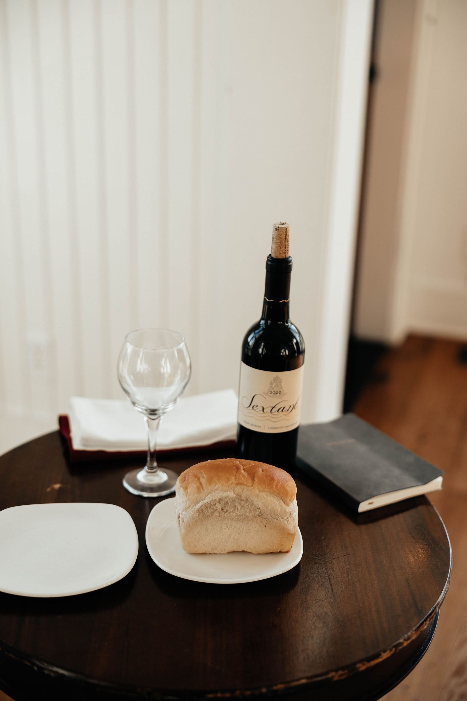 Wine bottle, empty glass, bread loaf, and Bible on wooden table for wedding ceremony.