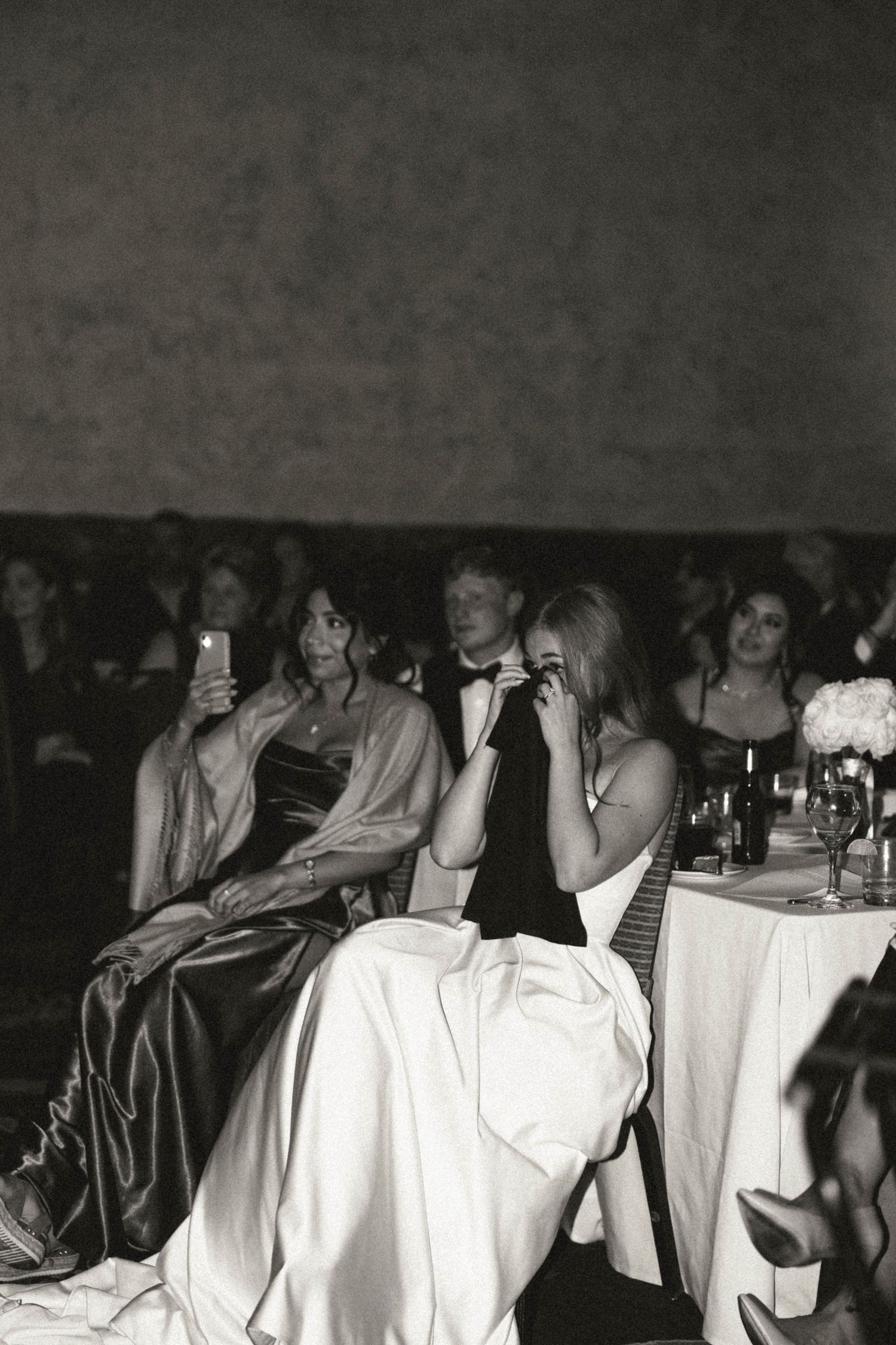 Black and white photo of wedding guests watching emotional moments during the reception program.