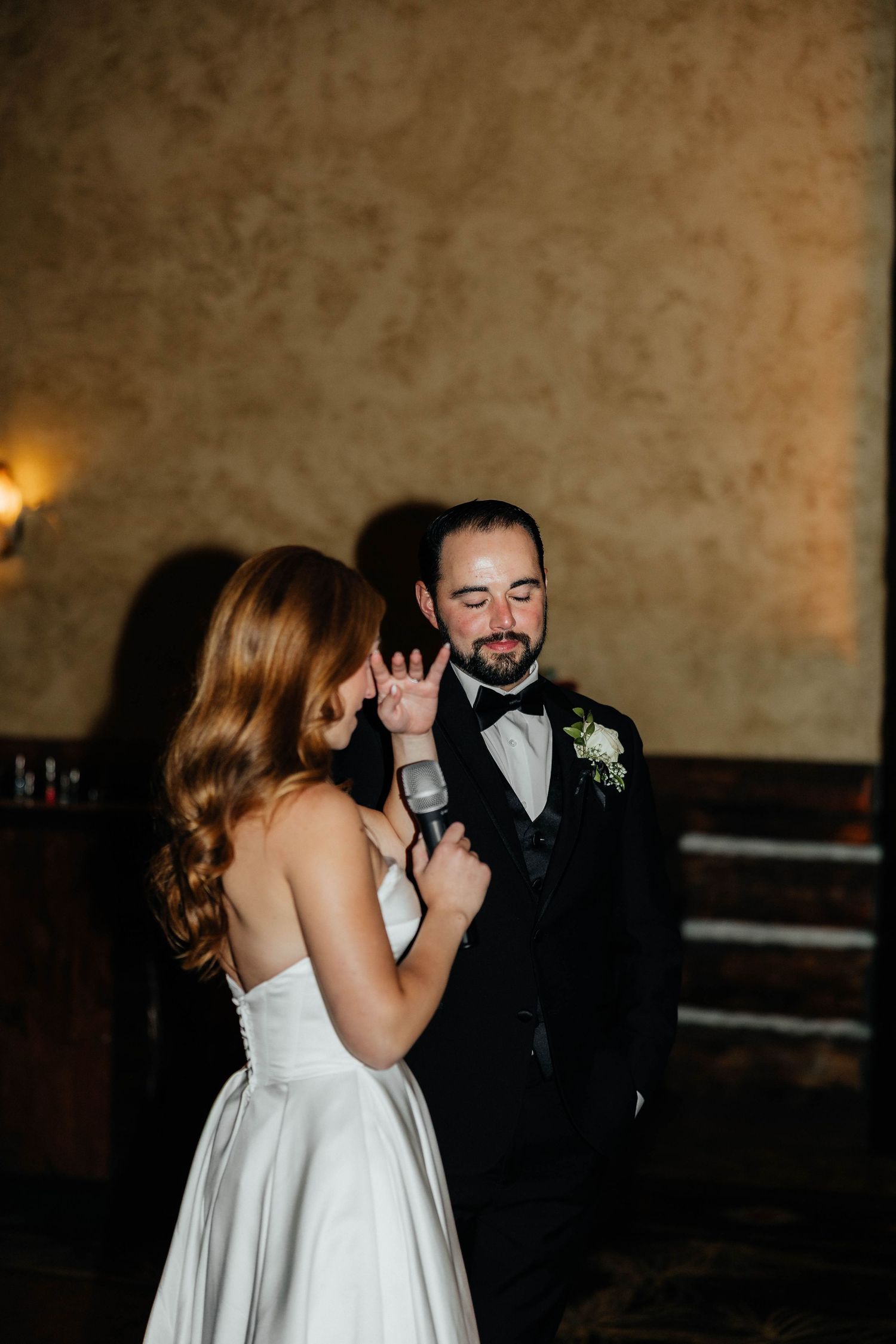 Bride tenderly touching grooms face during their first dance at wedding reception.