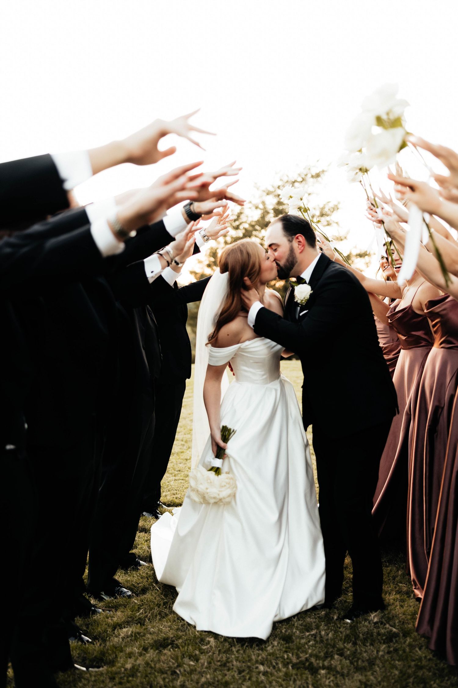 Bride and groom kissing under an arch of raised hands formed by their wedding party.