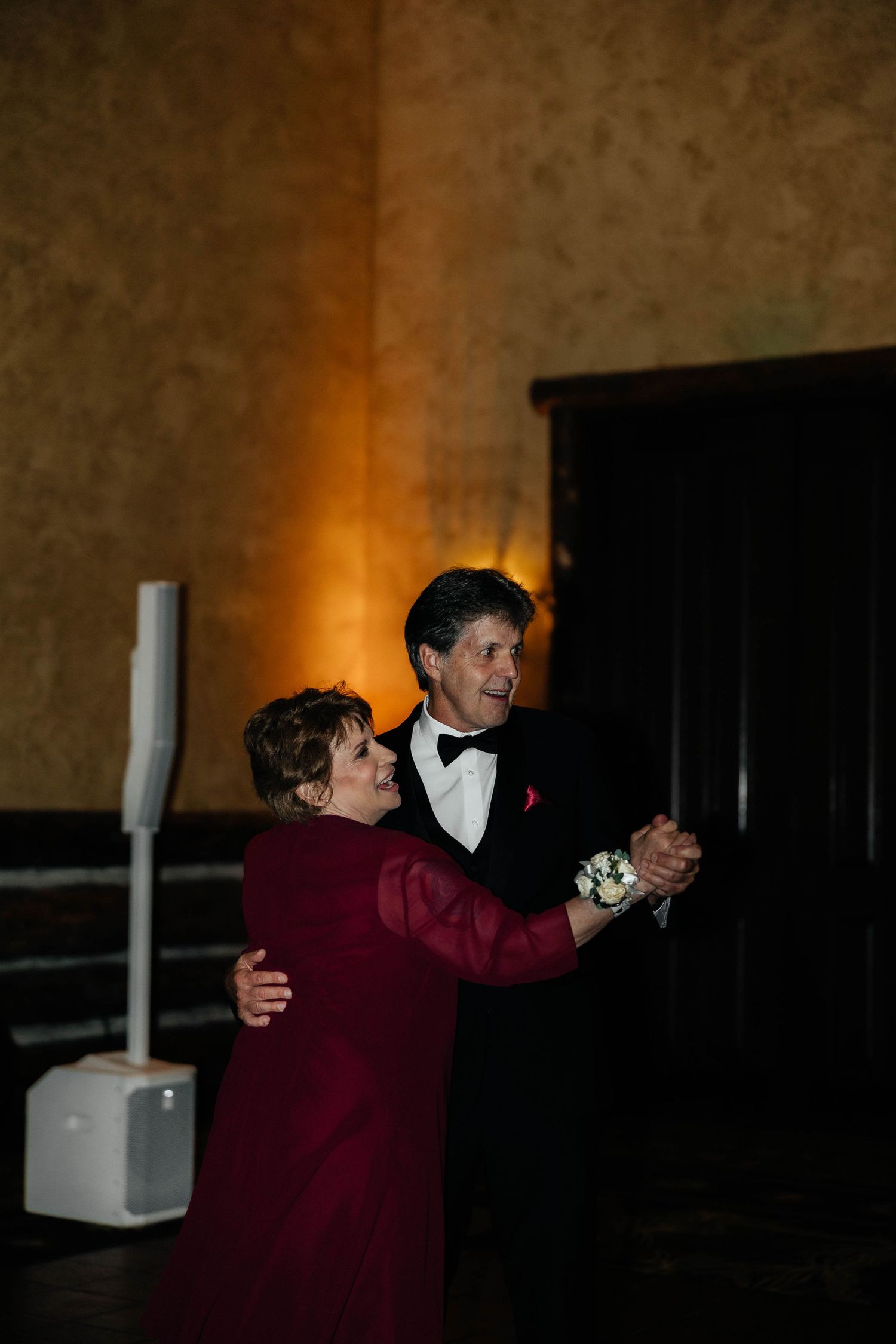 Older couple sharing a romantic dance at a wedding reception in warm amber lighting.