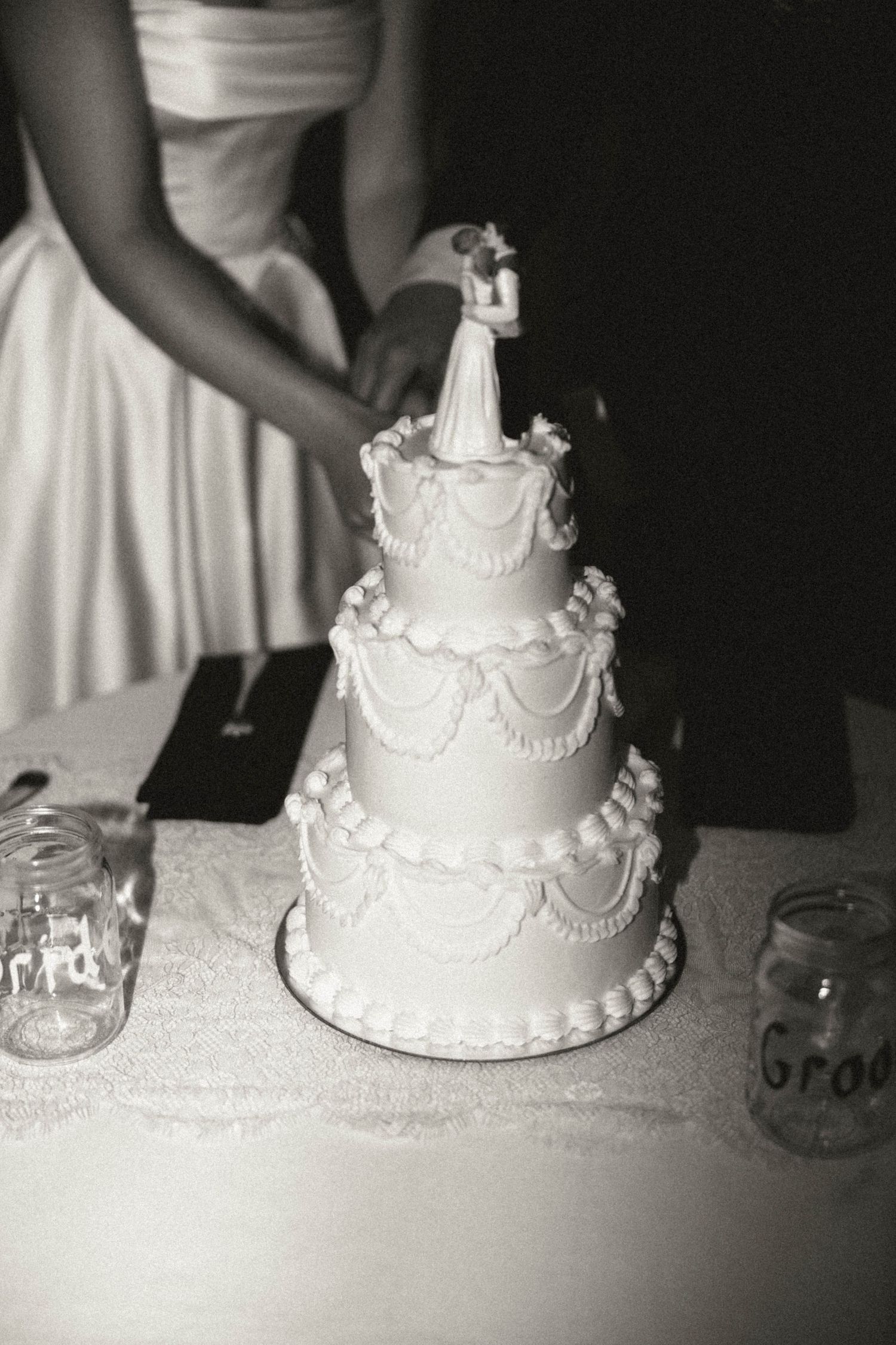Black and white close-up of elegant four-tier white wedding cake with bride and groom topper.