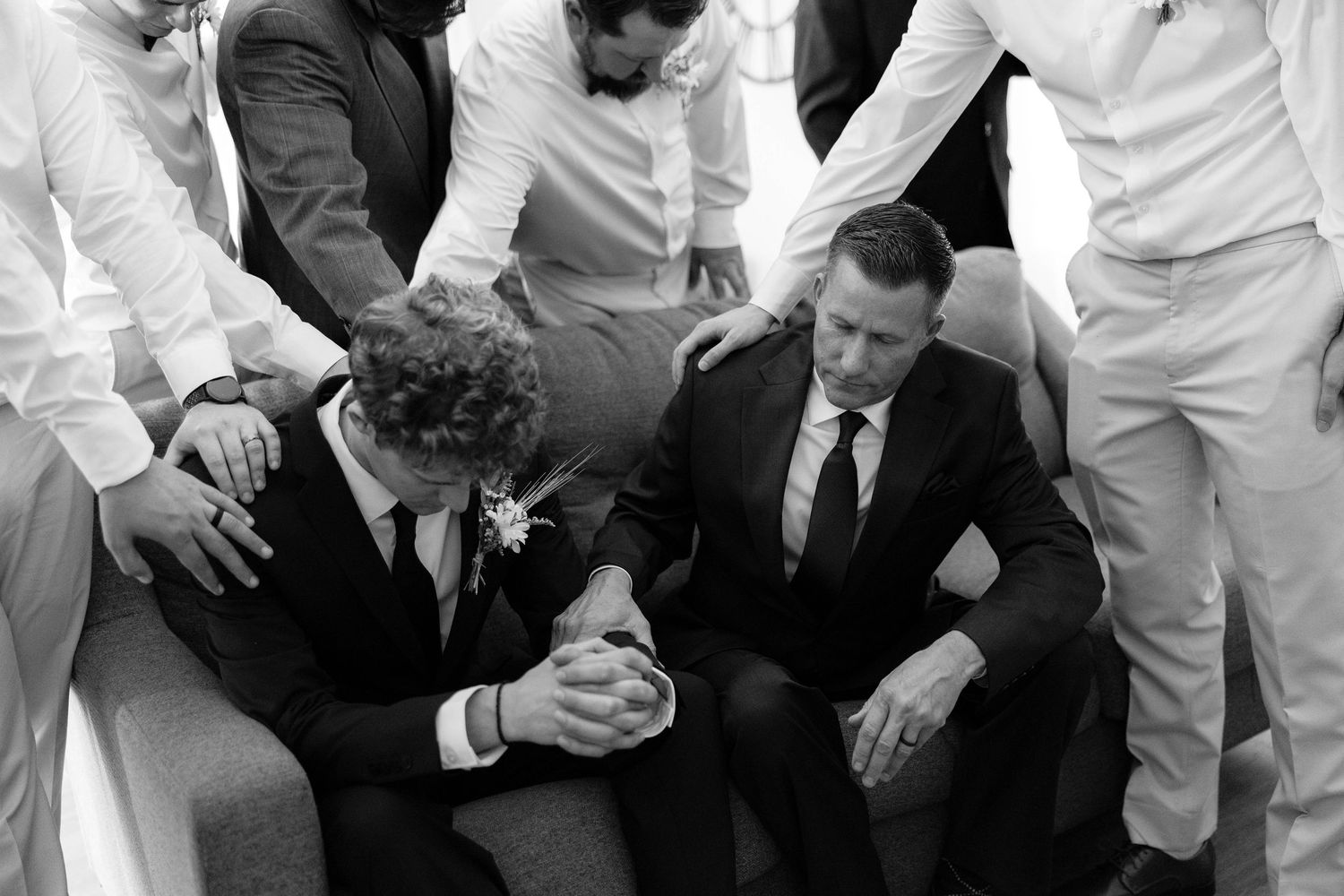 Black and white photo of groomsmen praying together before wedding ceremony.