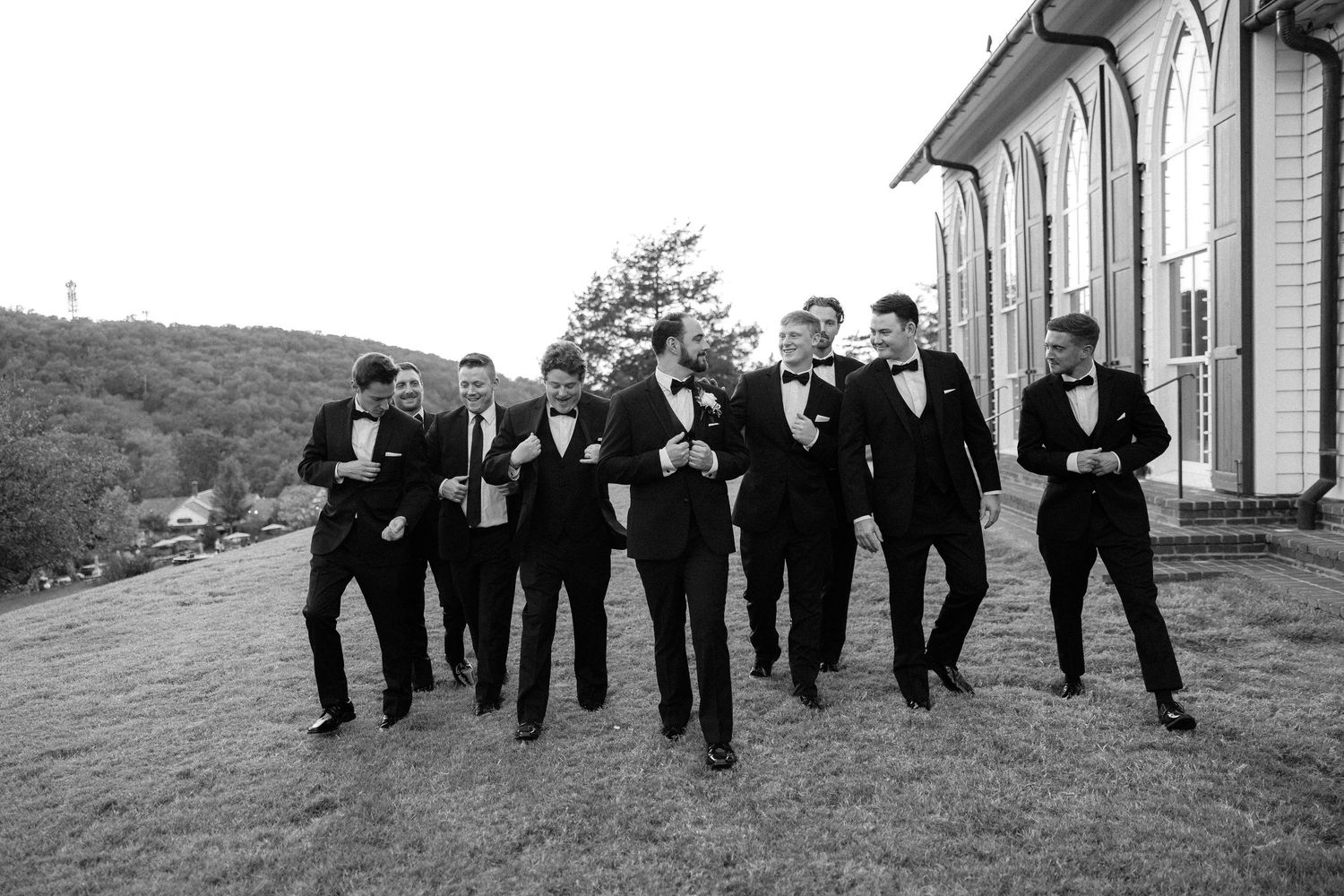 Groomsmen in black tuxedos walking together outdoors in black and white wedding photo.