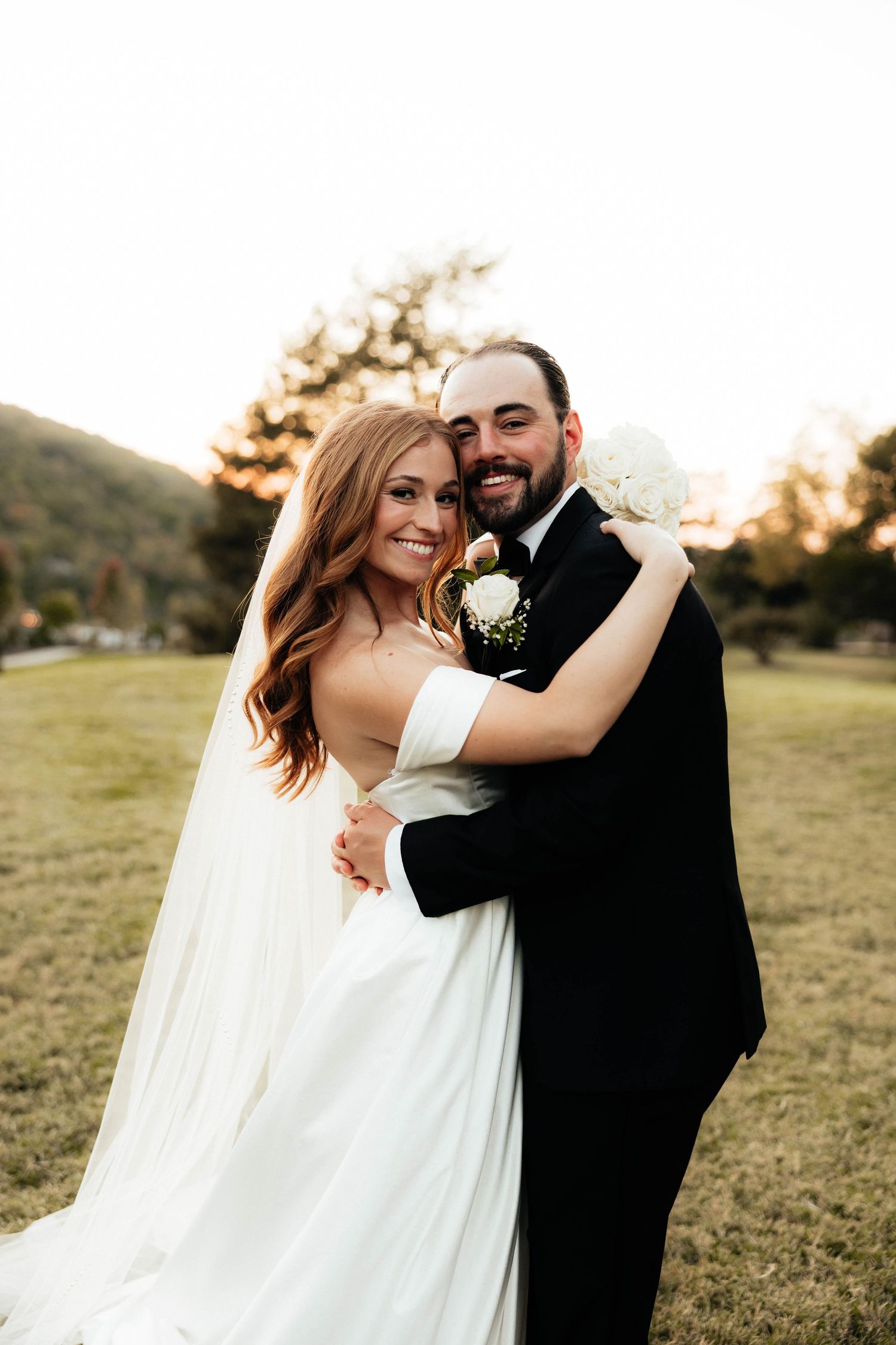 Happy bride and groom posing together at sunset with scenic mountain landscape behind them.