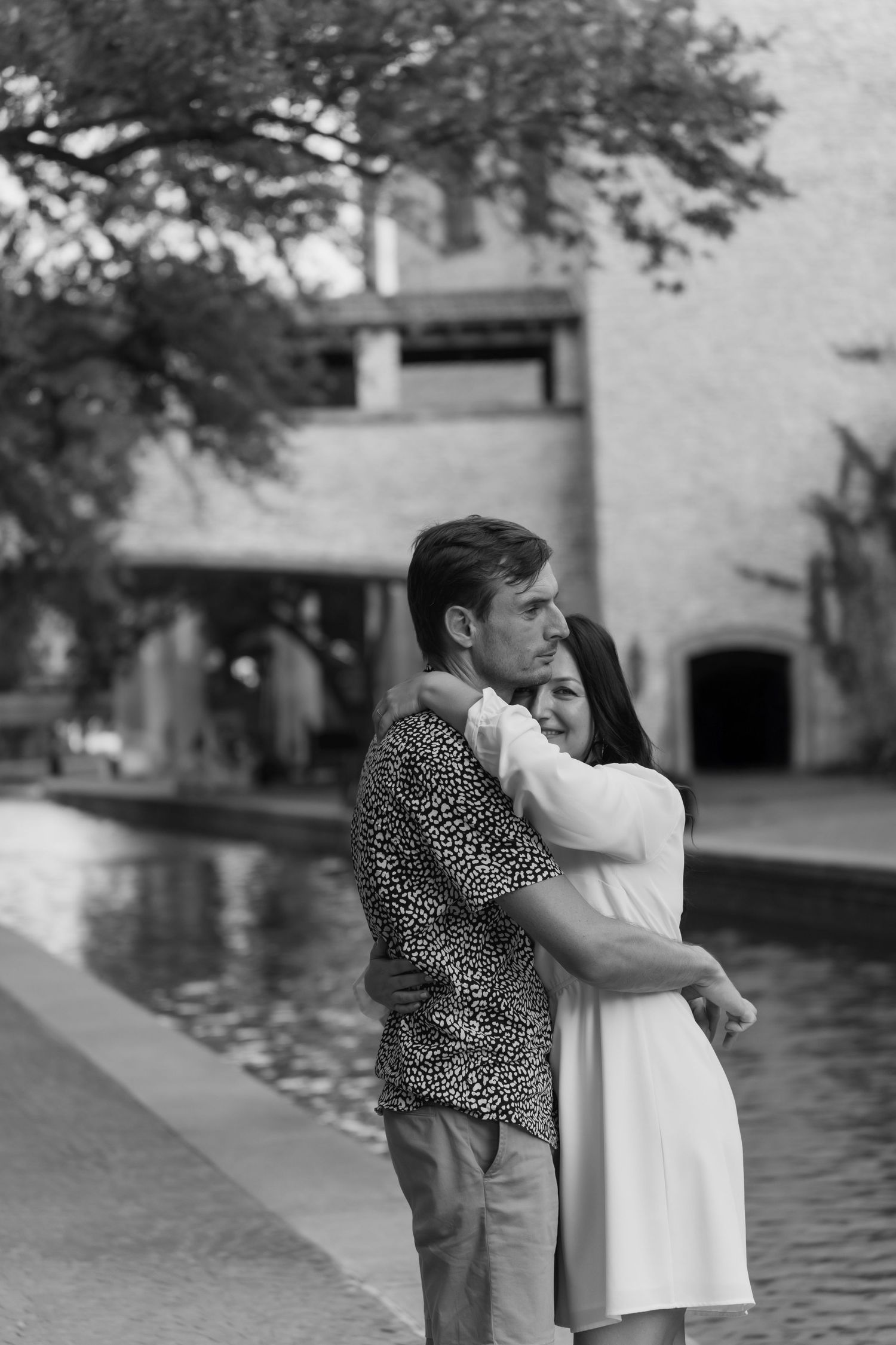 Black and white portrait of a couple sharing intimate moments near a reflecting pool.