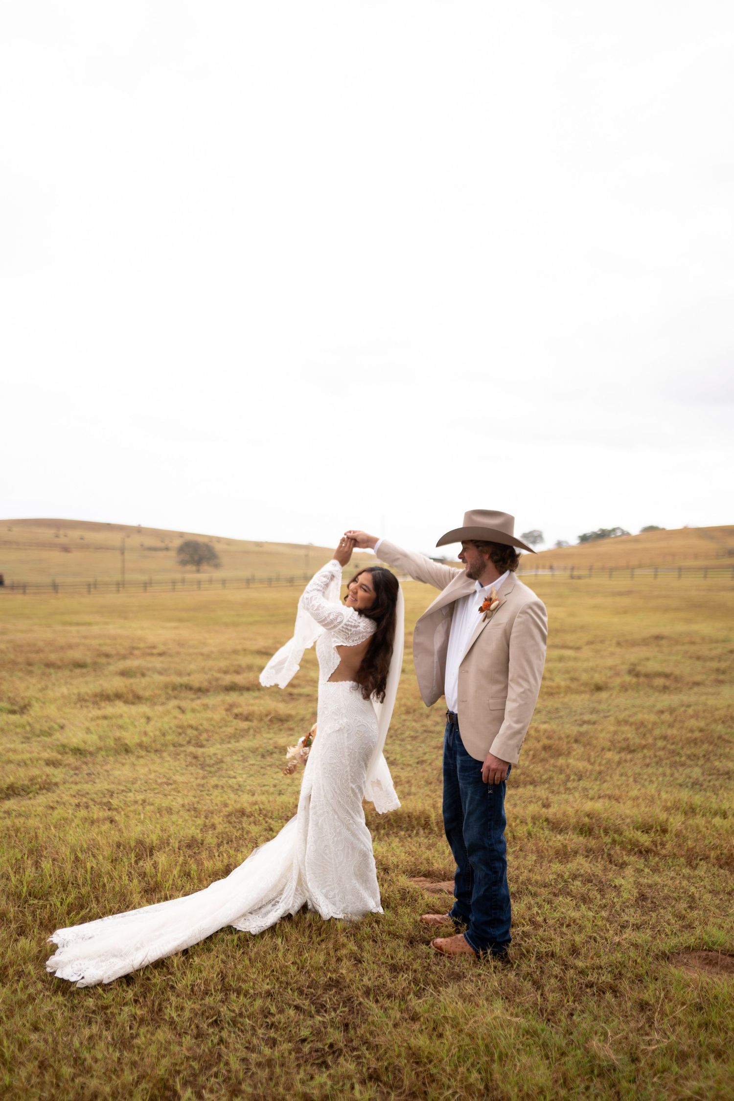 Couple in western wedding attire poses romantically in golden field at sunset.