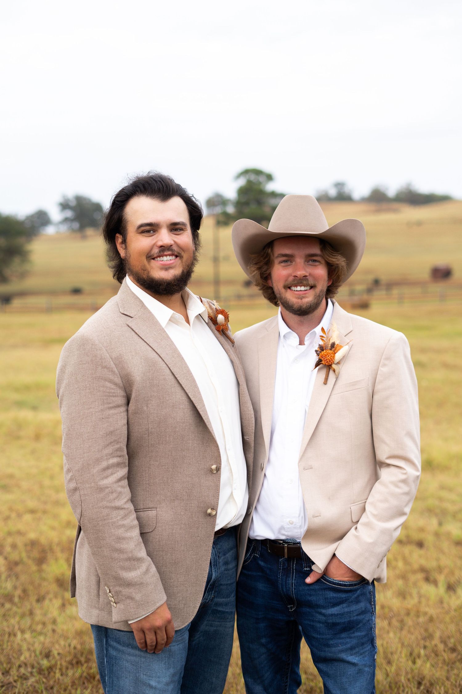 Groomsmen in tan suits and cowboy hats posing in outdoor field setting.