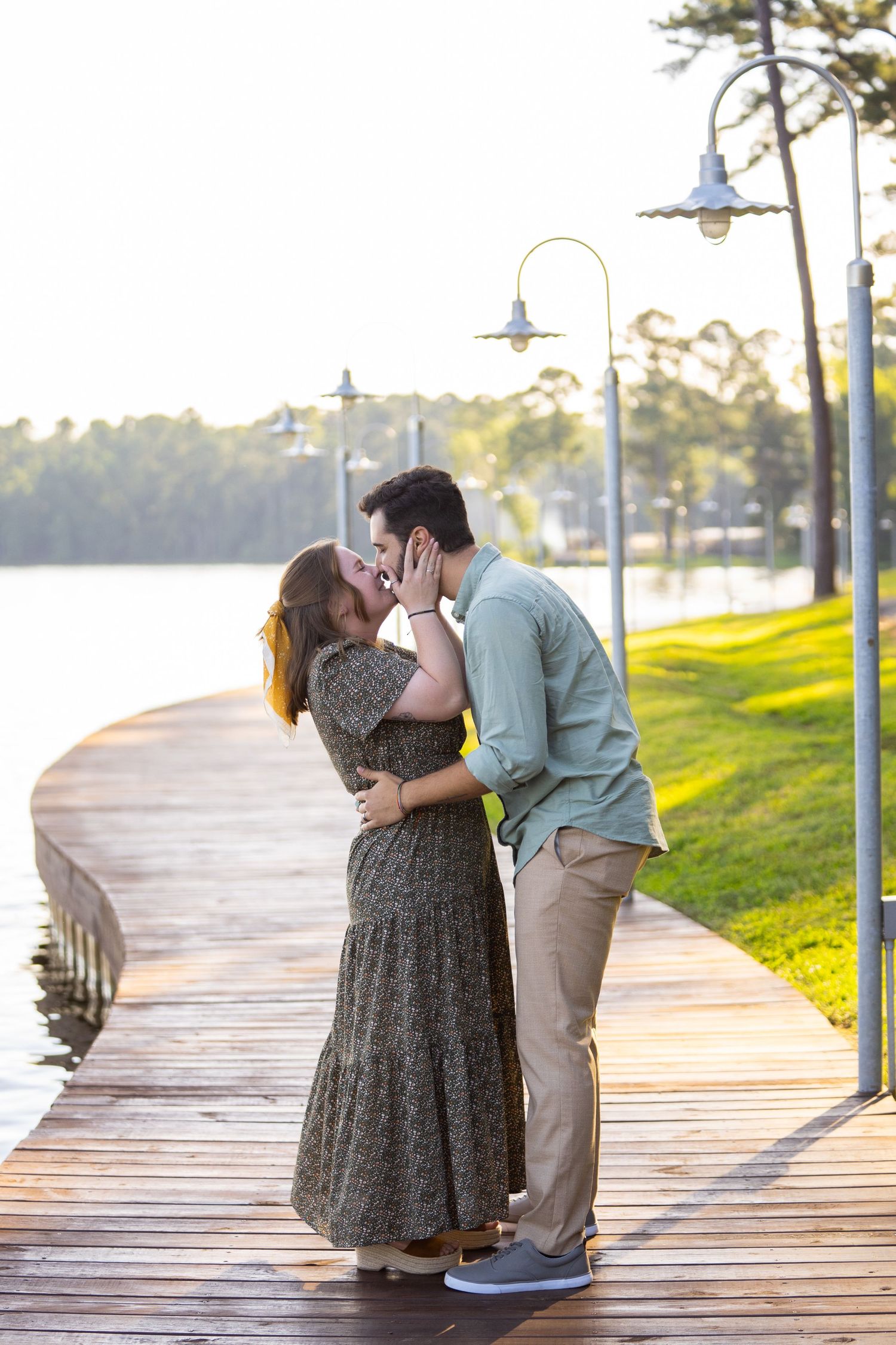 A couple embraces on a lakeside boardwalk during a romantic sunset moment.