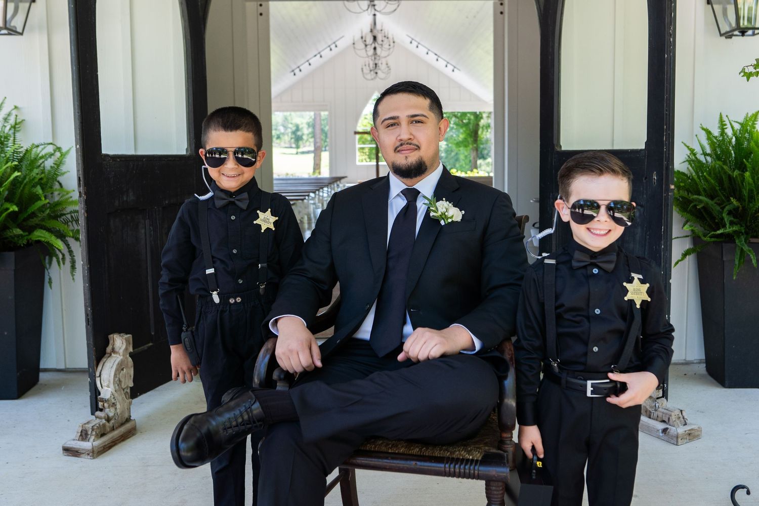 Groomsmen in black suits strike fun poses in a series of wedding party photos outside a building.