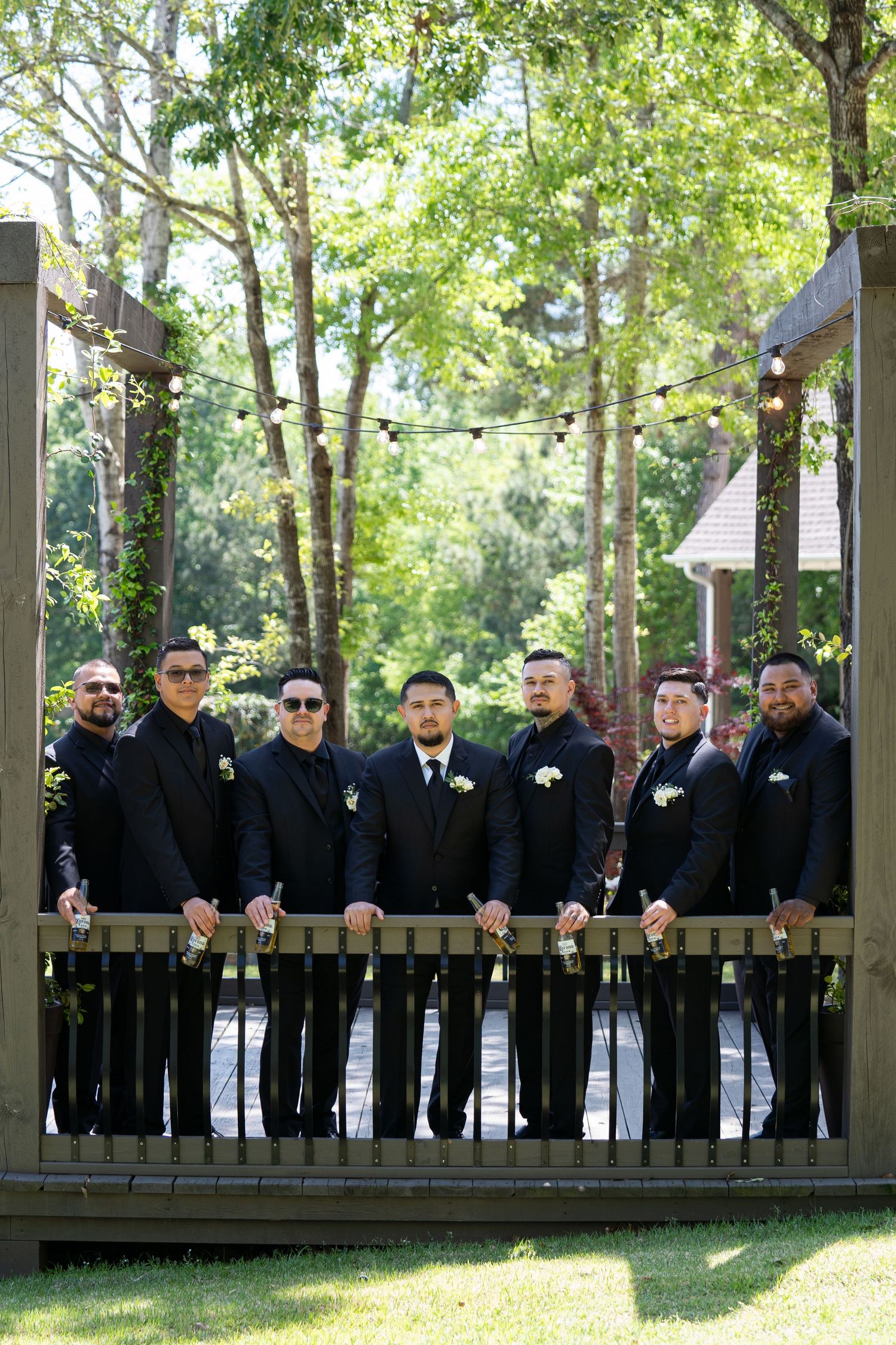 A group of people wearing black shirts and sunglasses stand in a line on a wooden deck surrounded by trees.