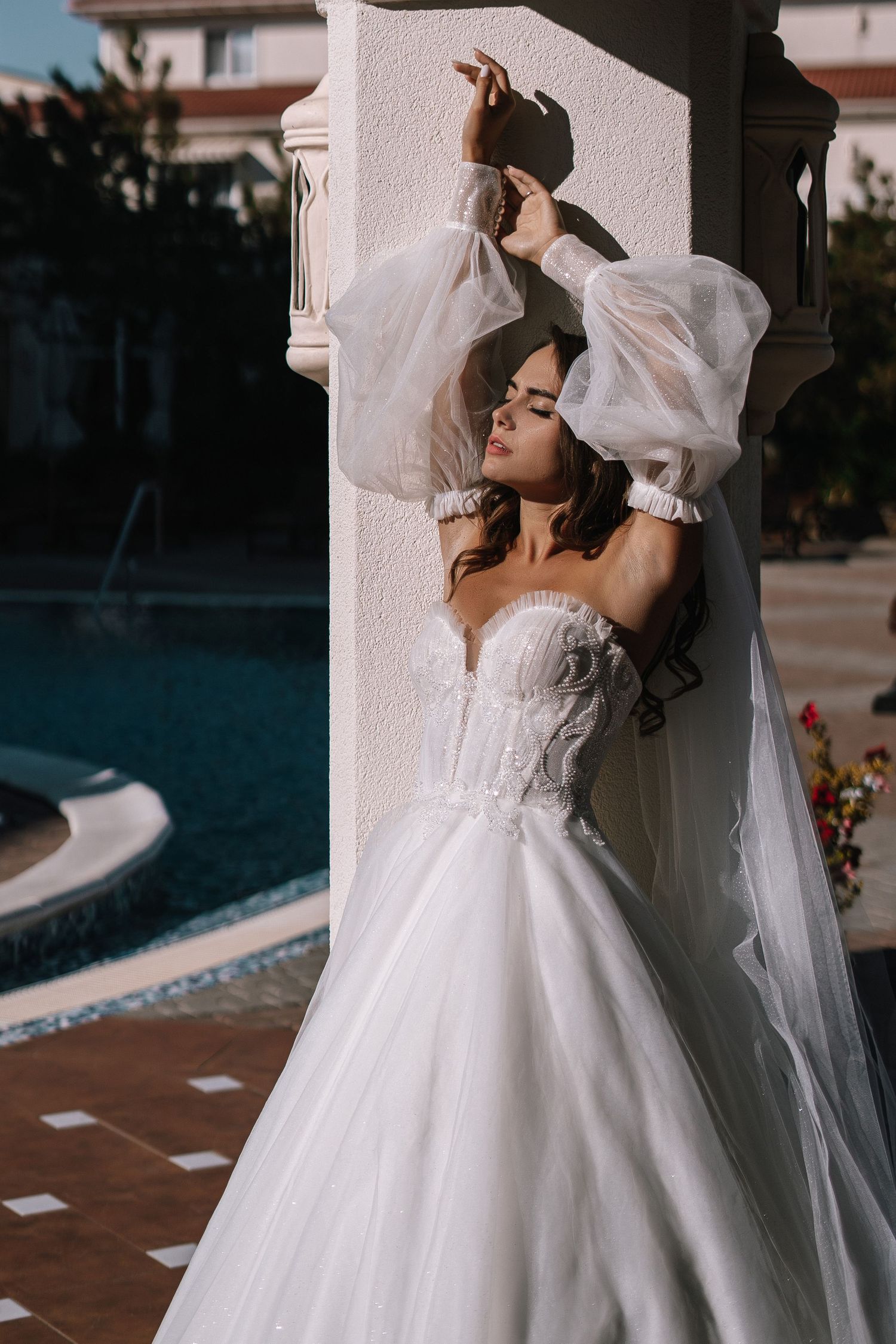 A romantic wedding couple embraces in a series of intimate poses wearing traditional white wedding attire by a pool.