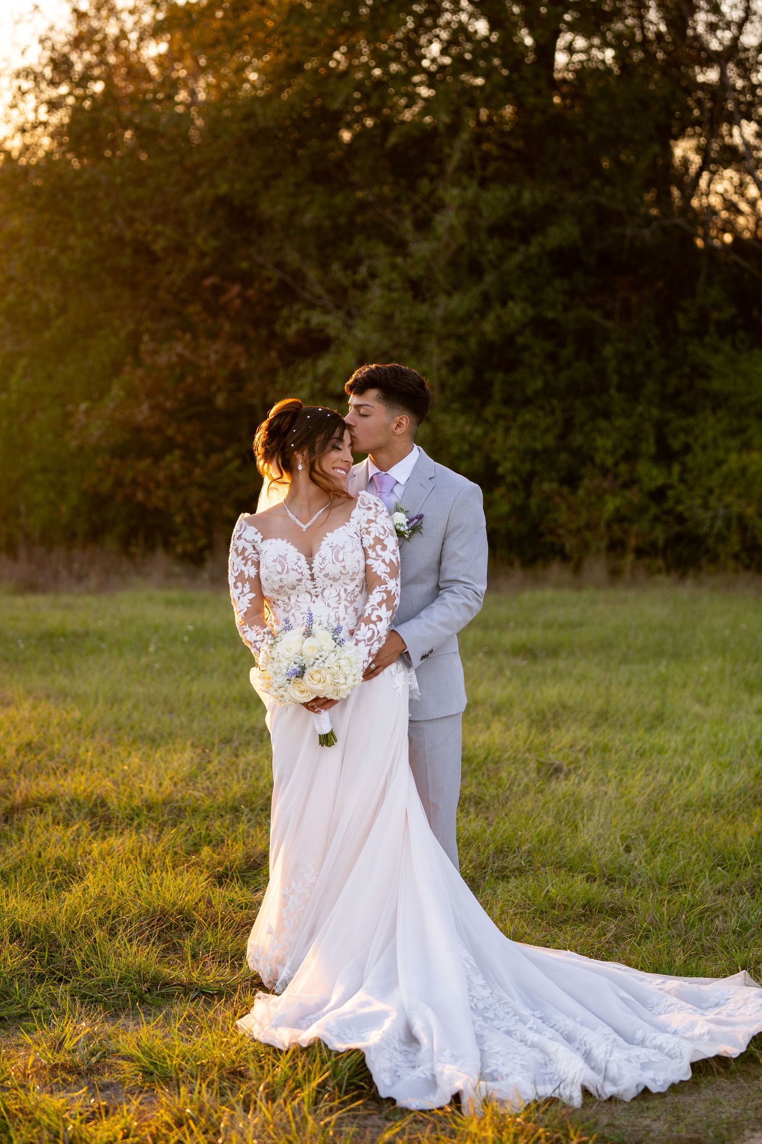 Wedding couple shares intimate moment in field during golden hour photography session.