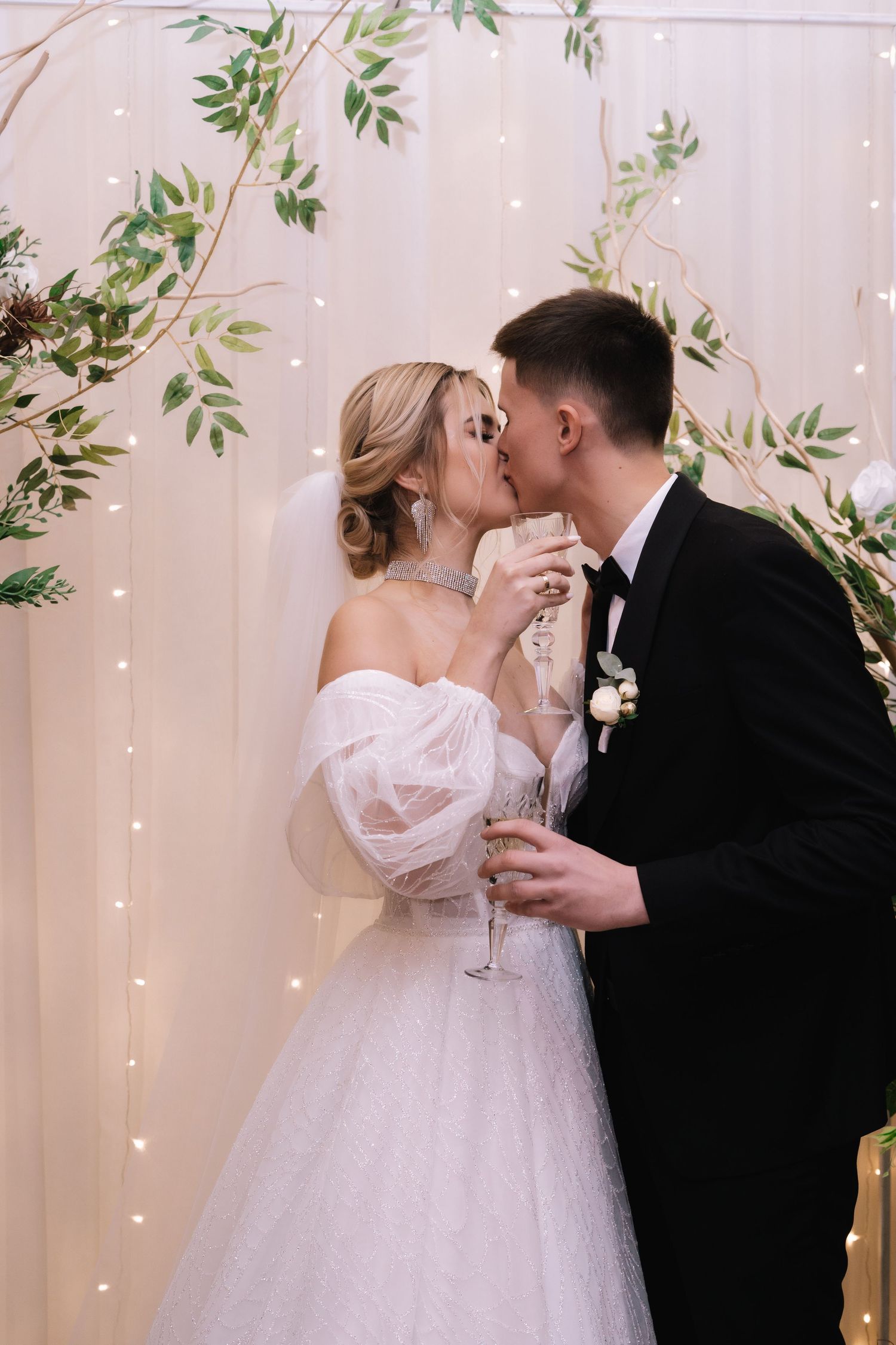 Four sequential photos show a romantic wedding kiss between newlyweds against a backdrop of twinkle lights and greenery.