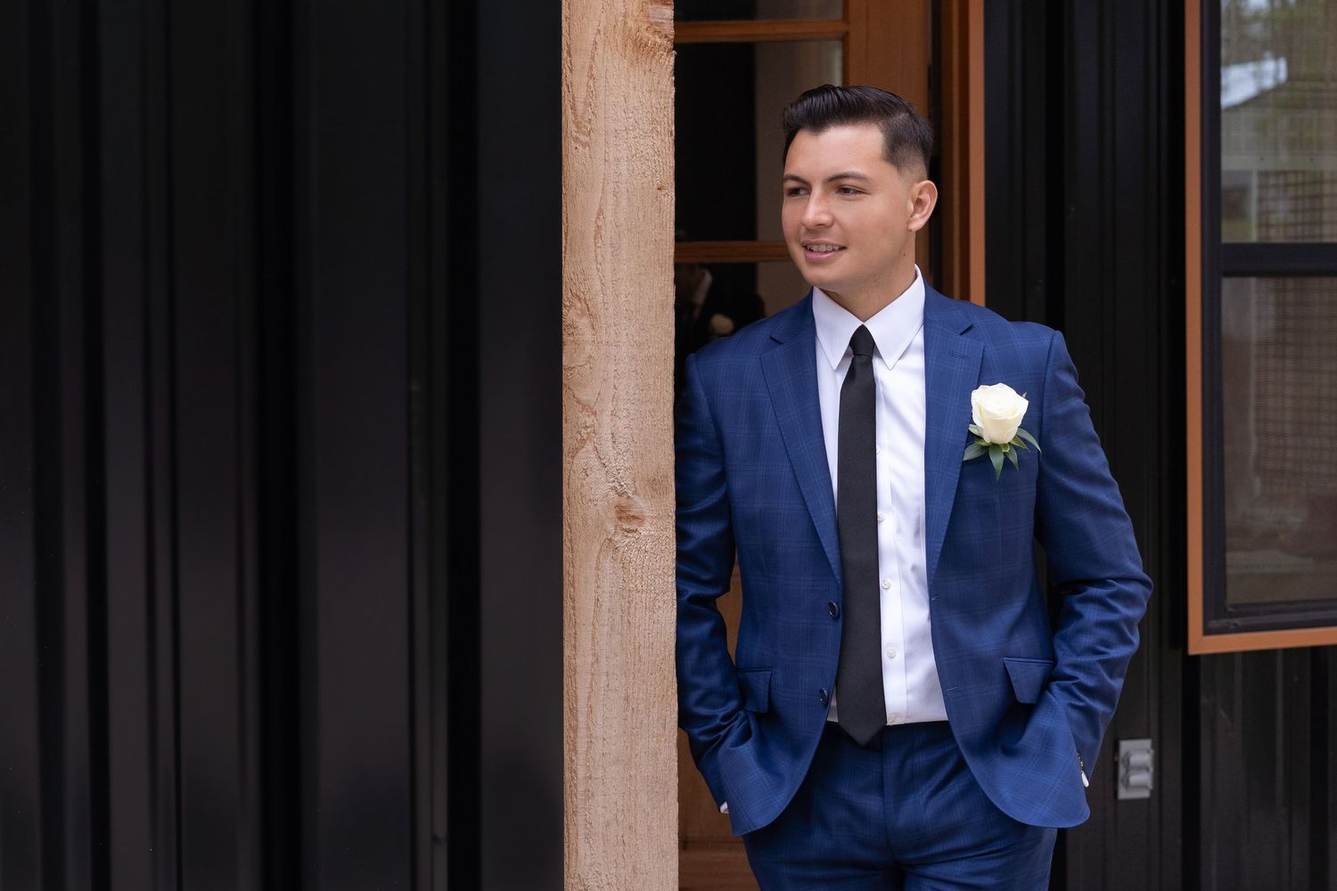 A person in a navy blue suit and white tie stands confidently against a dark background.