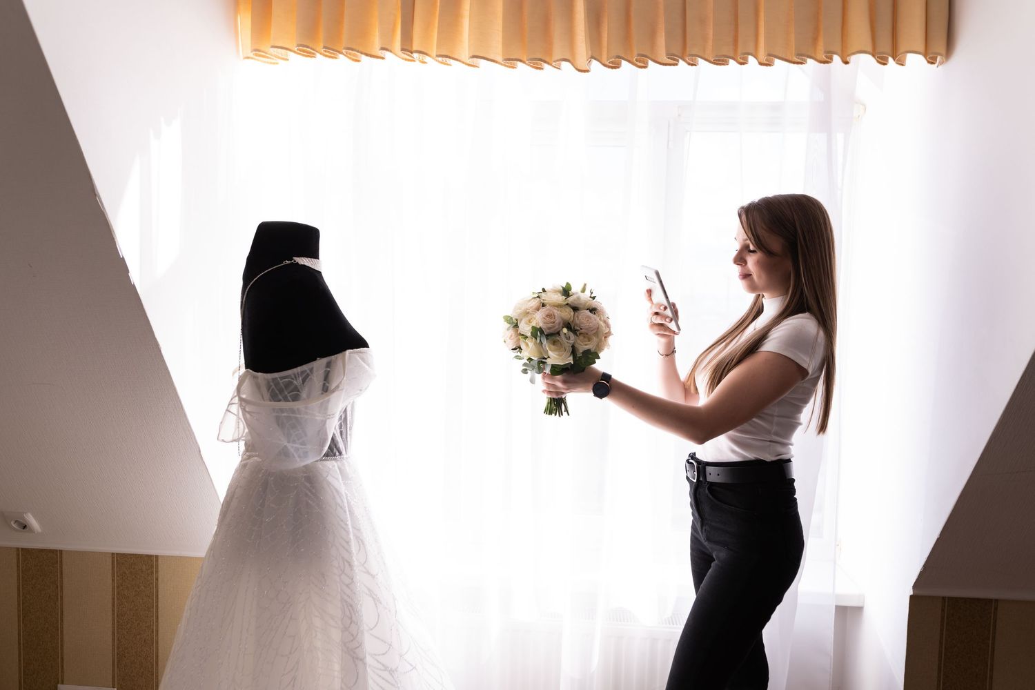 A photographer captures a behind-the-scenes moment with a wedding dress displayed while taking photos in a bright room.