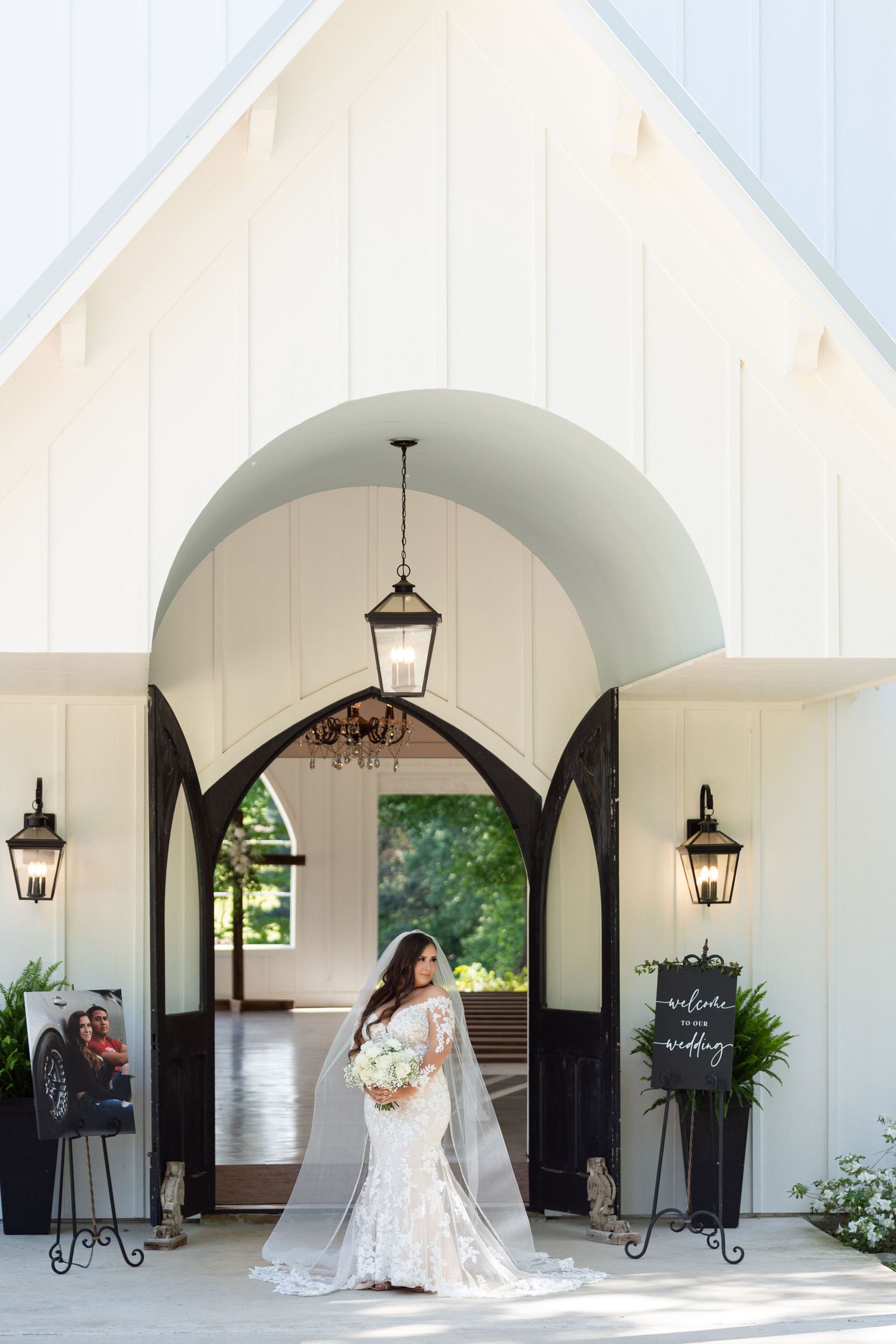 A series of elegant white archways with hanging lanterns create a romantic covered walkway at a wedding venue.