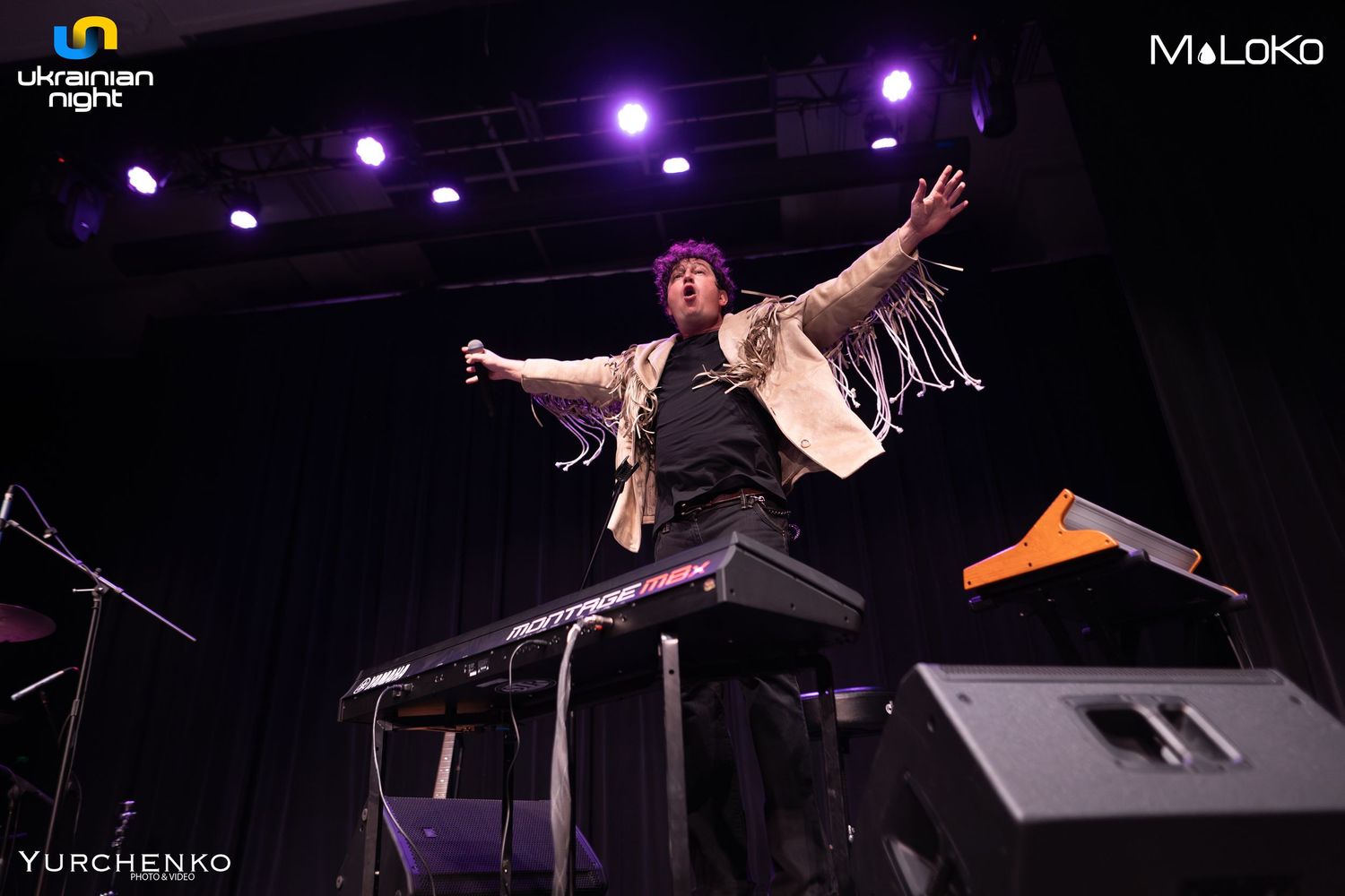 Stage performers in dynamic poses under purple theatrical lighting during live show.