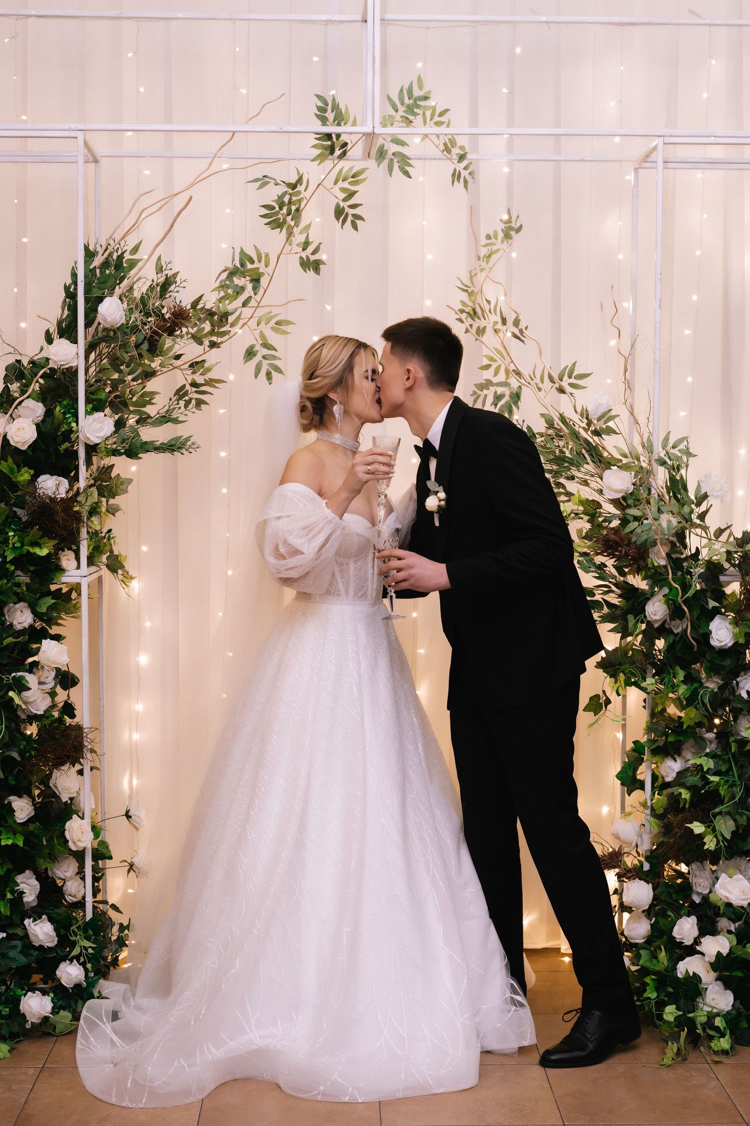 A romantic wedding scene with a couple sharing a moment under floral arches and twinkling lights.