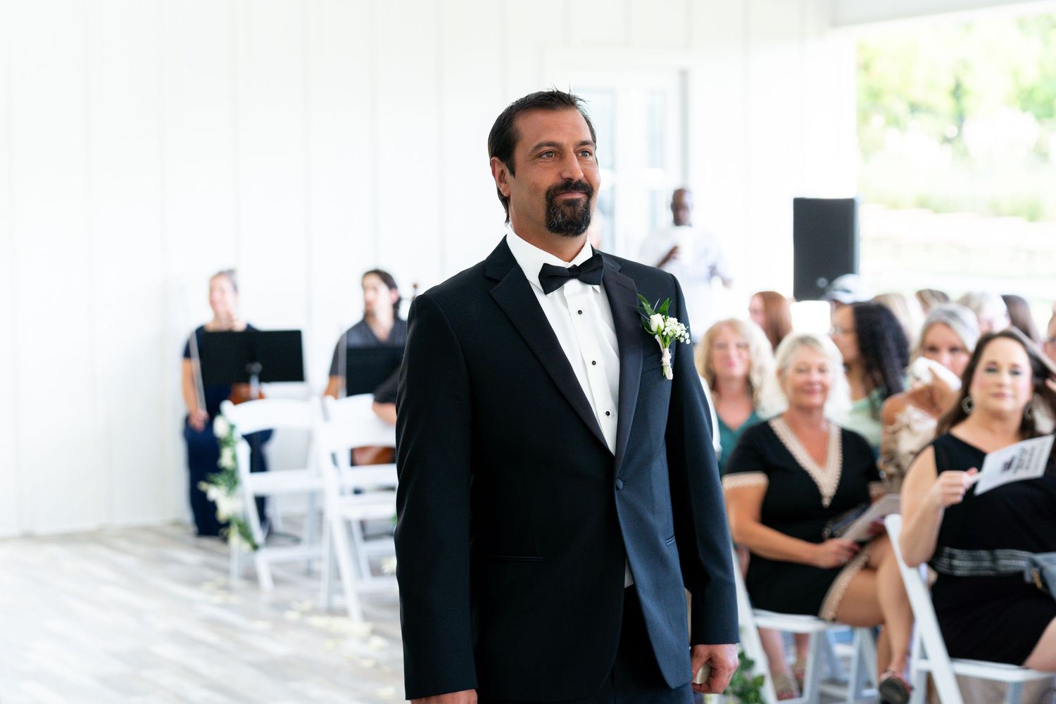 A person in a black tuxedo and bow tie stands at attention during a formal wedding ceremony.