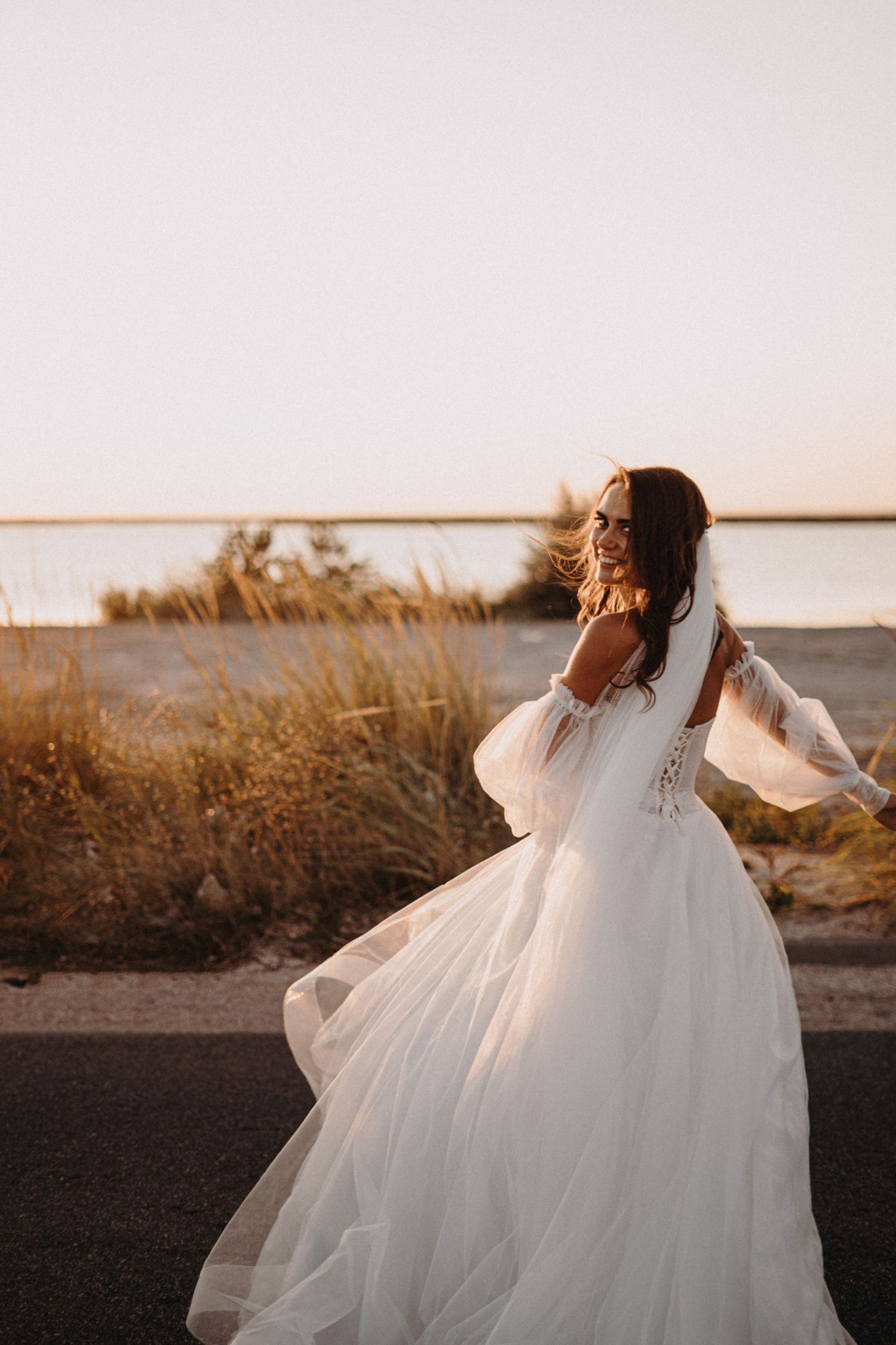 A flowing white wedding dress twirls gracefully during golden hour sunset at a waterfront location.