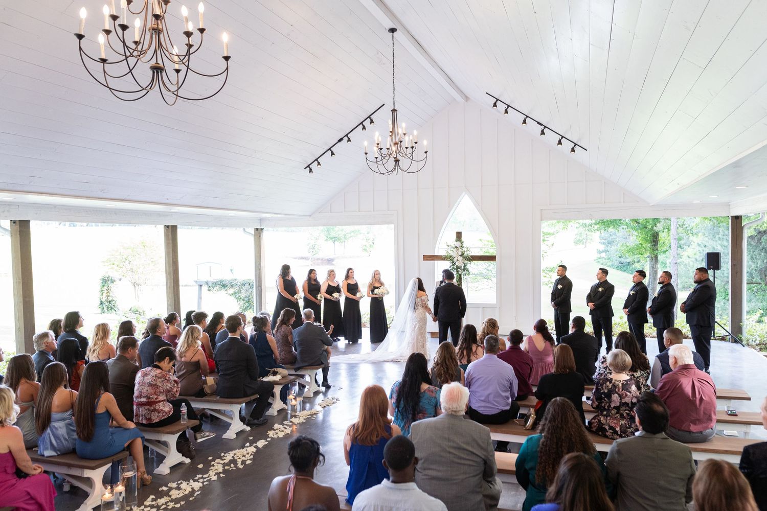 People gathered in a white tent venue for a formal event with chandeliers and table settings.