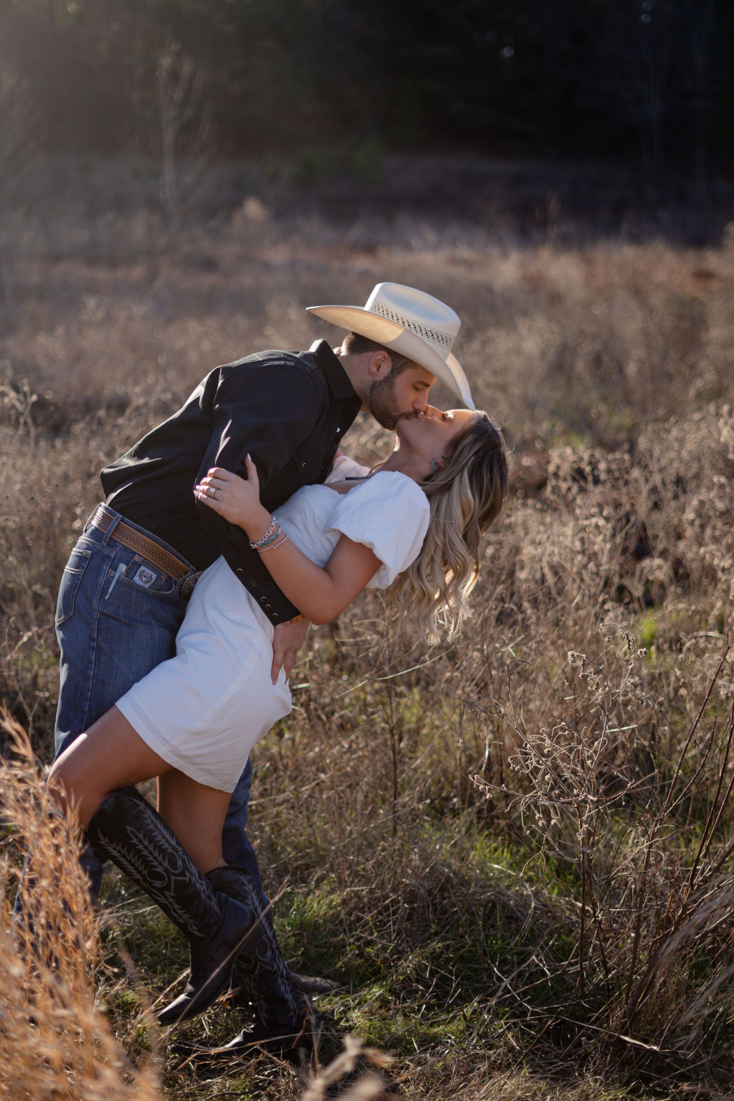 Romantic couple embracing in a field of dried grass during golden hour.