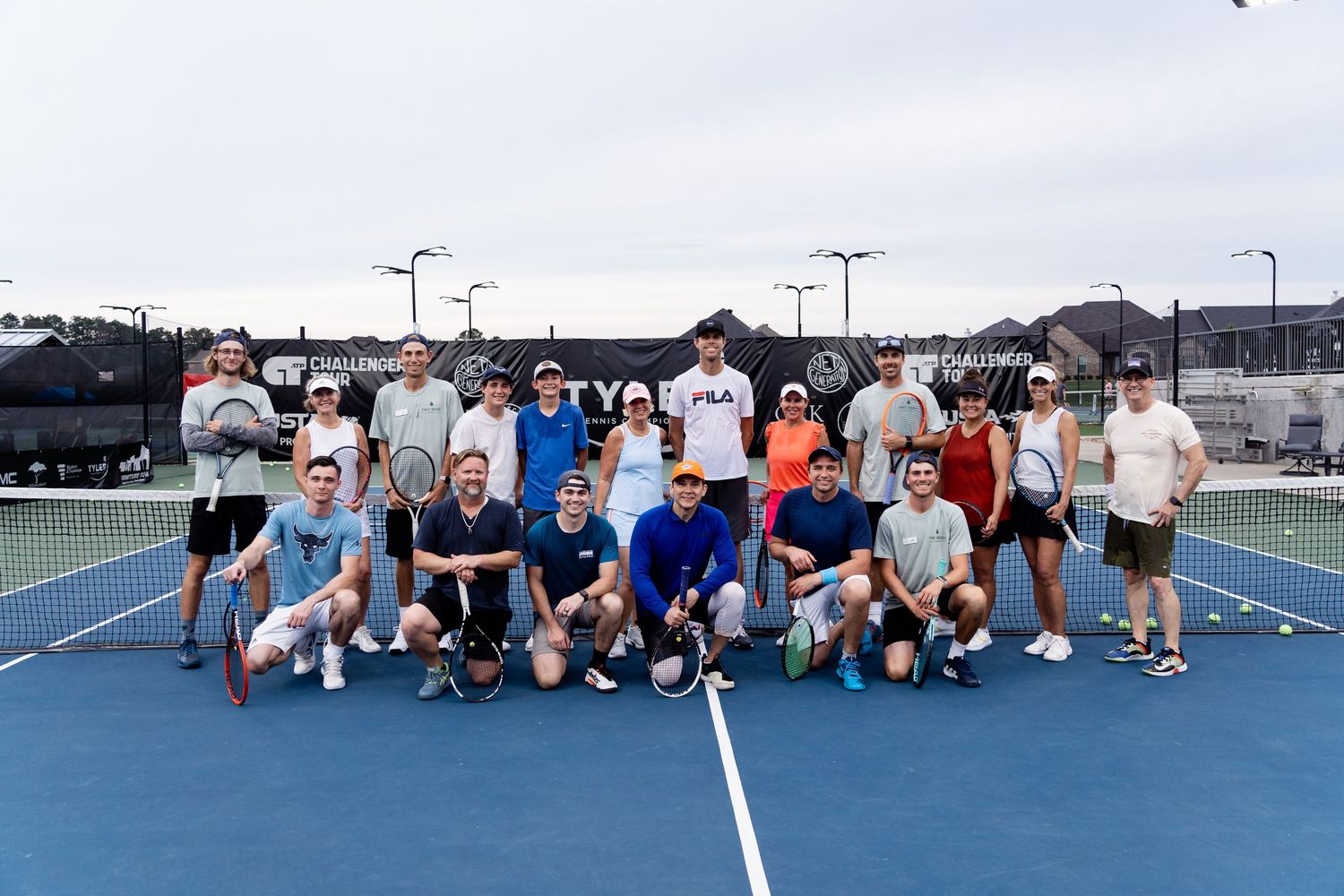 Large group of tennis players posing together on outdoor tennis courts.