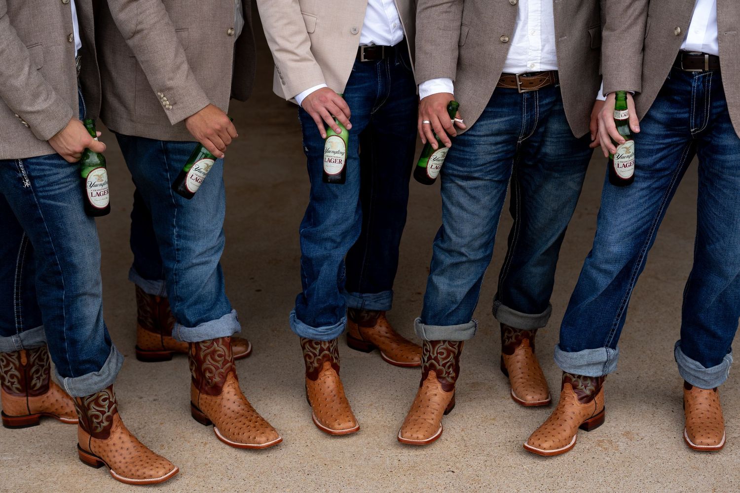 Row of groomsmen showing off matching brown leather boots with rolled up jeans.