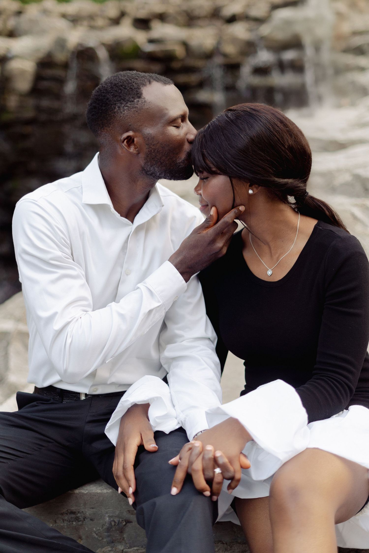 Couple sharing tender moments while sitting on rocky terrain.