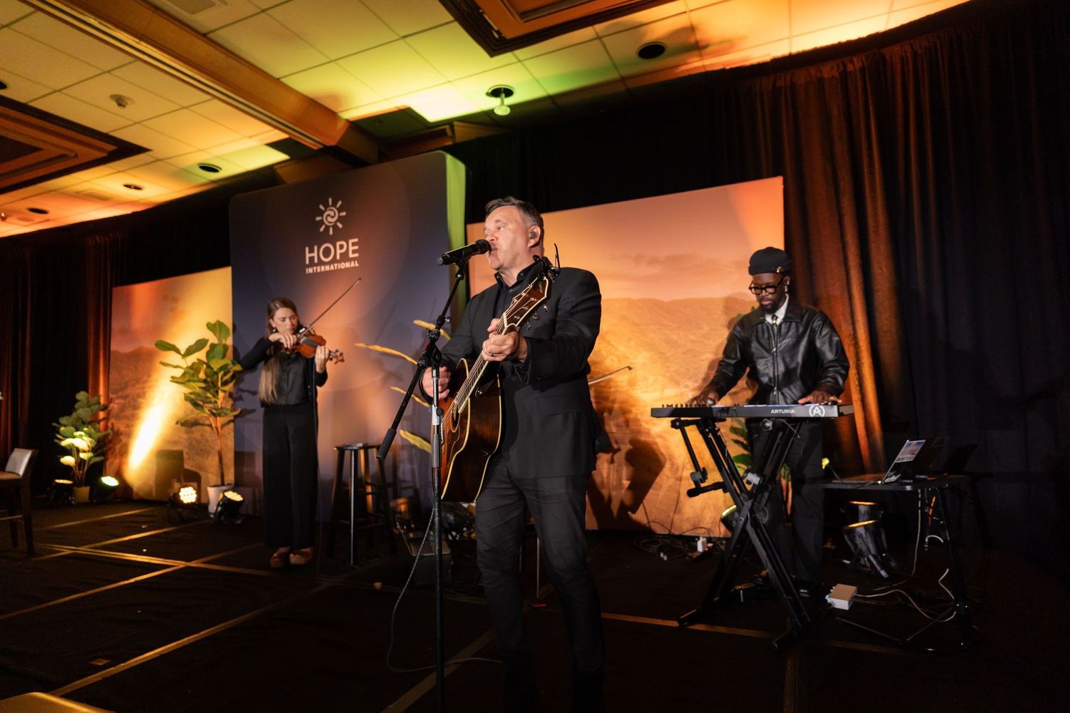Band performing on stage with dramatic lighting at evening event.
