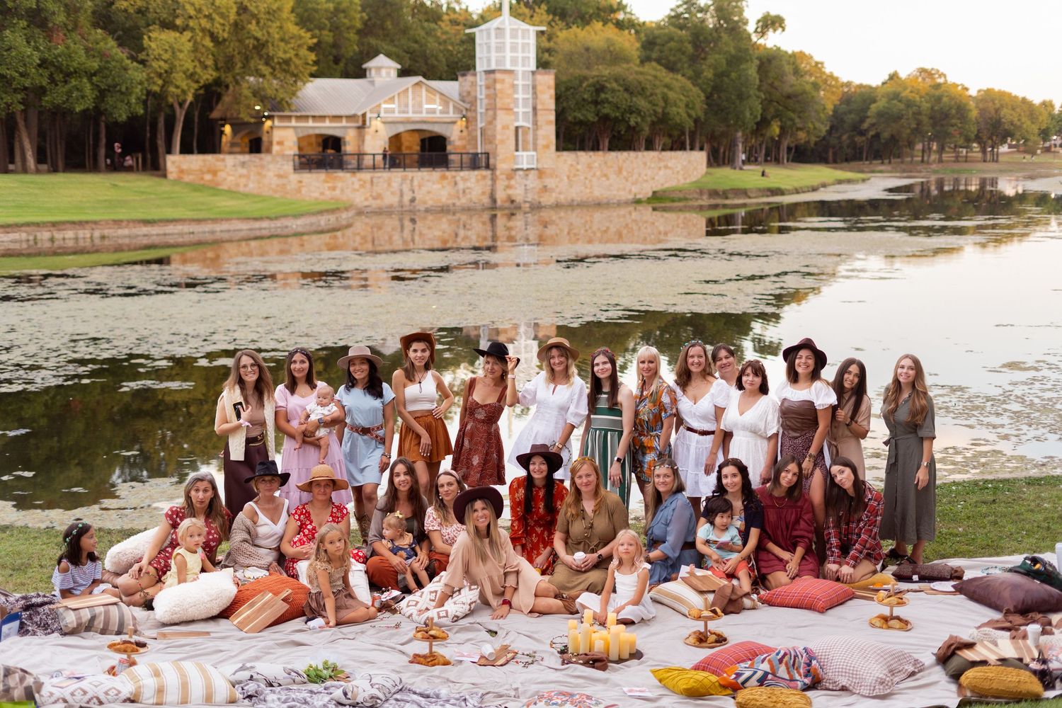 Large group picnic gathering on a grassy lawn near historic buildings at sunset.