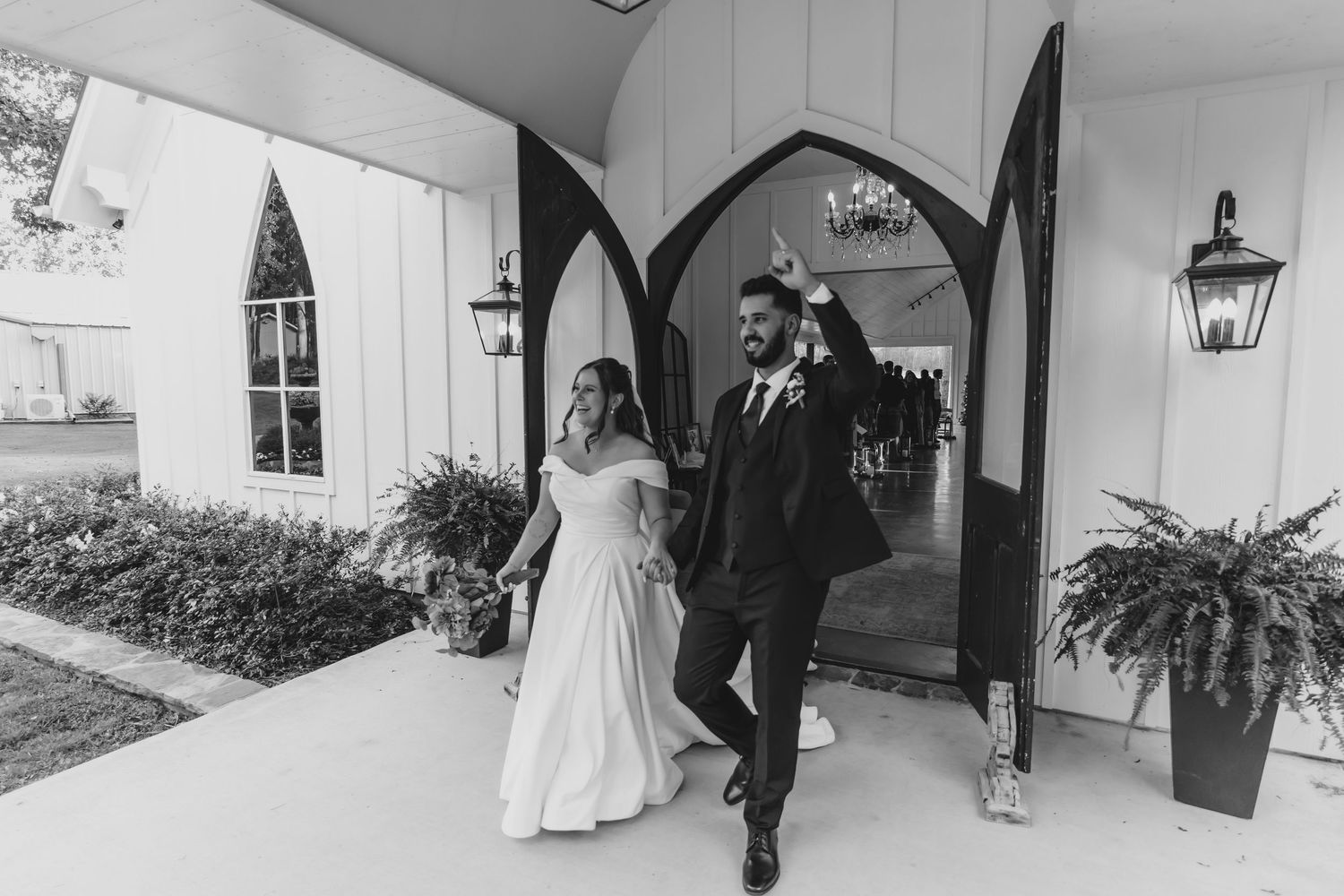A black and white photo of newlyweds exiting their wedding venue through an arched doorway.