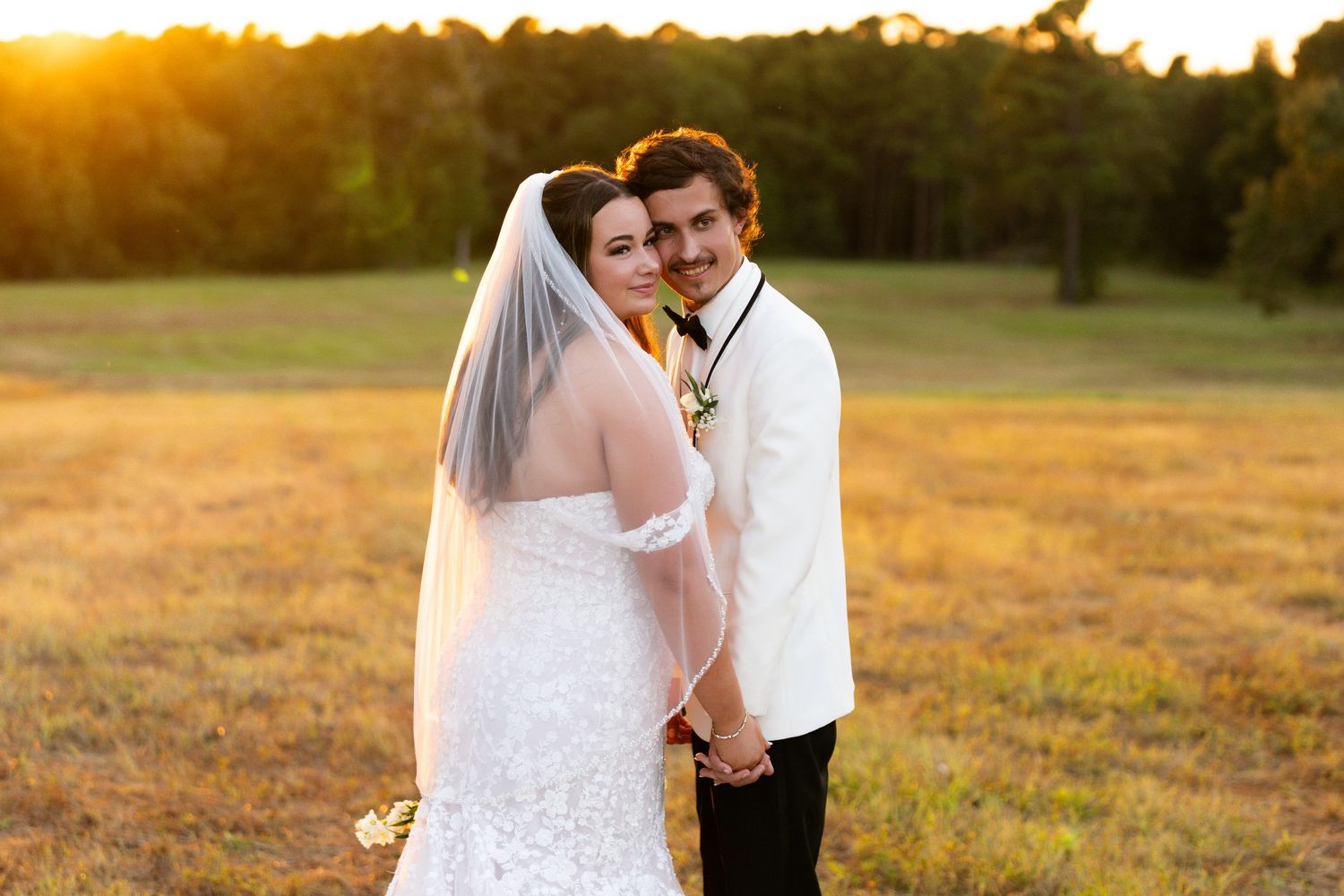 A couple in wedding attire embraces in a golden field at sunset during their romantic outdoor photo session.