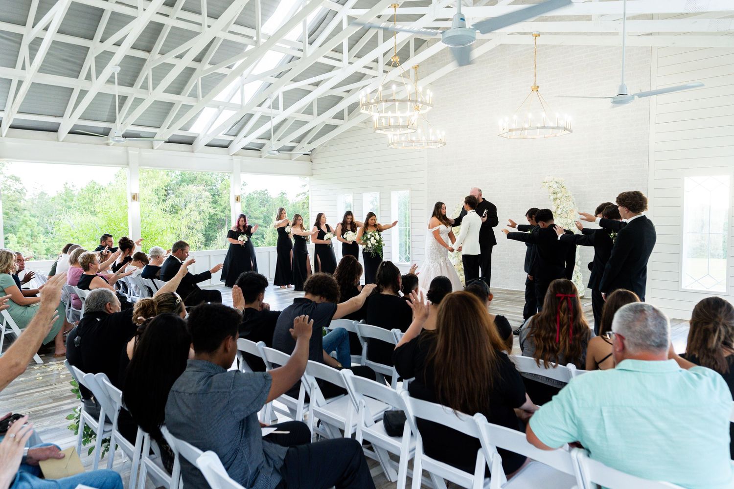 Wedding guests stand and celebrate during an indoor reception ceremony under a white tent structure.