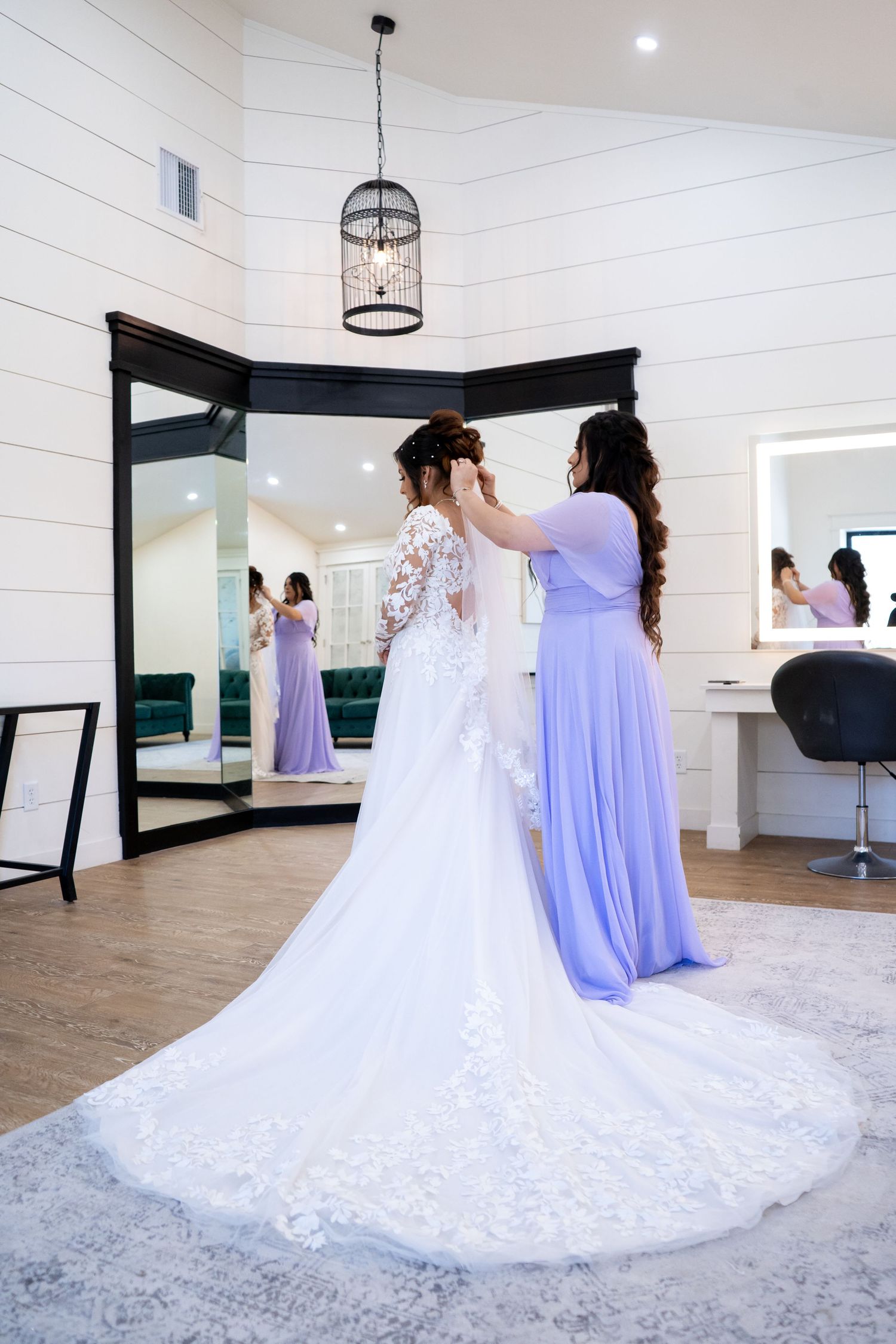 A wedding dress with intricate lace detail and long train being adjusted in a bridal suite.