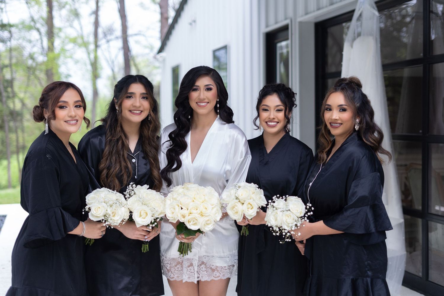 Bridesmaids in black dresses pose with white bouquets in an elegant wedding party photo shoot.