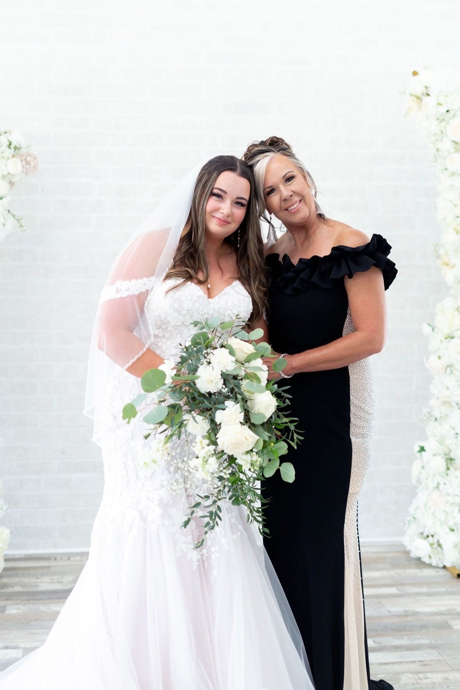 Wedding party poses together with white floral arrangements and decorations against a light colored wall.