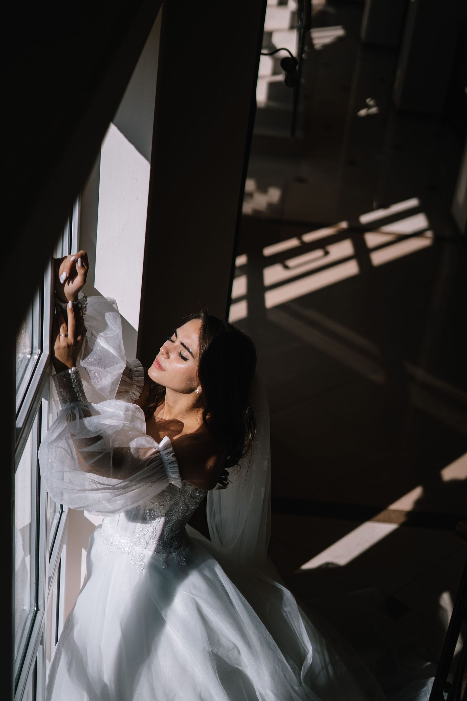 A person in a flowing white dress poses dramatically against a wall with shadows creating striking patterns.