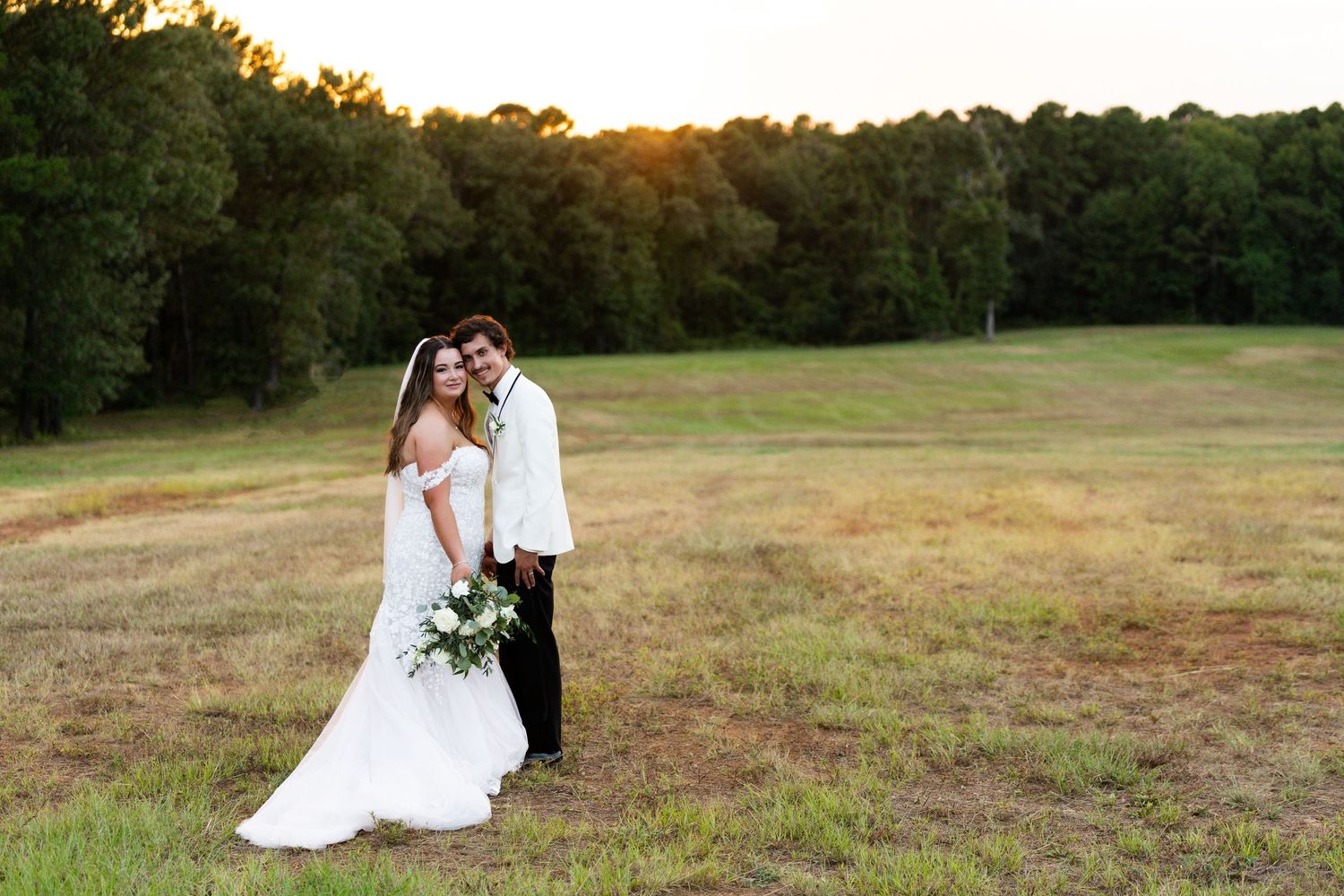 Romantic couple embraces in golden sunlit field during sunset photoshoot.