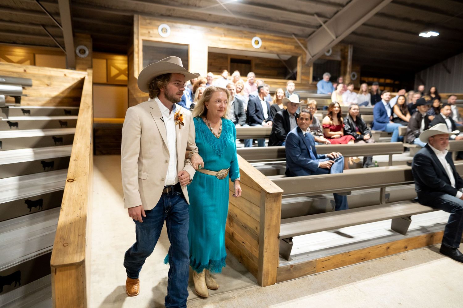Wedding guests seated in wooden bleacher-style seating at indoor venue.
