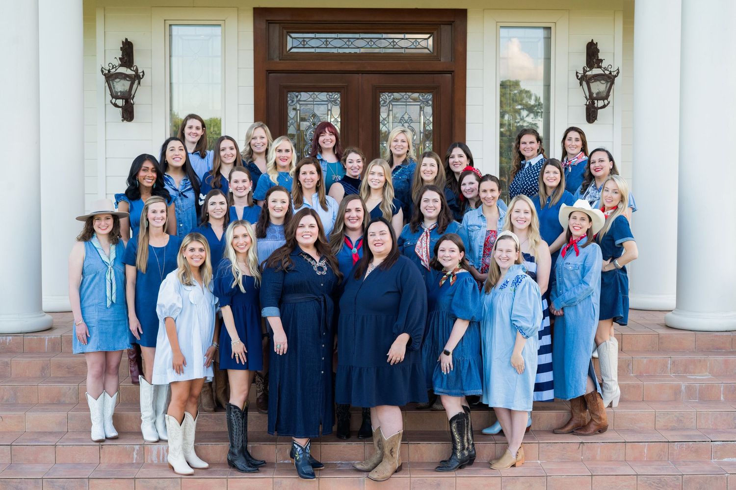 Group portrait of women in blue and black attire gathered on building entrance steps.